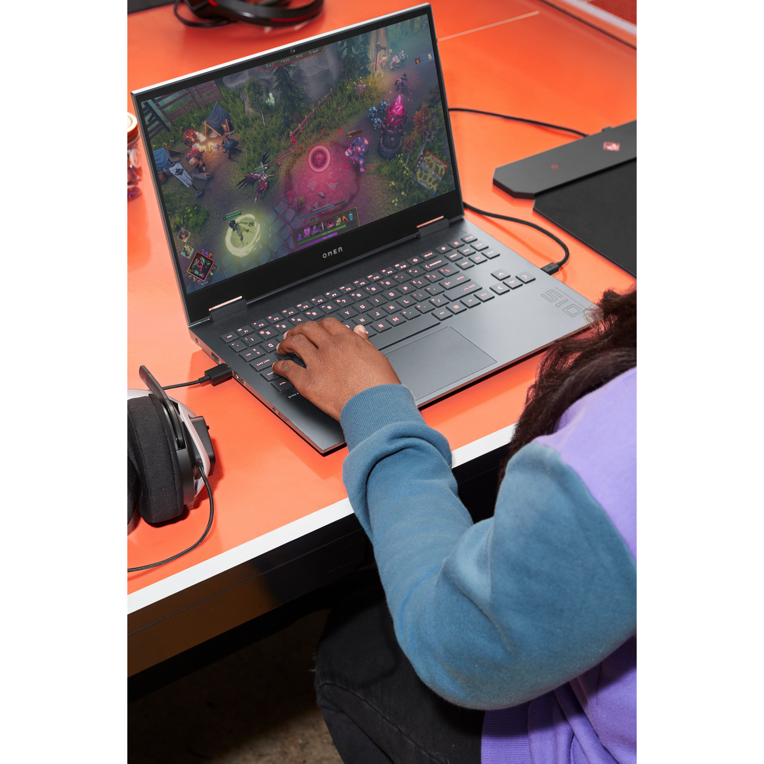 Una persona usa una laptop, jugando un juego. La pantalla muestra el juego, auriculares y un ratón cerca.