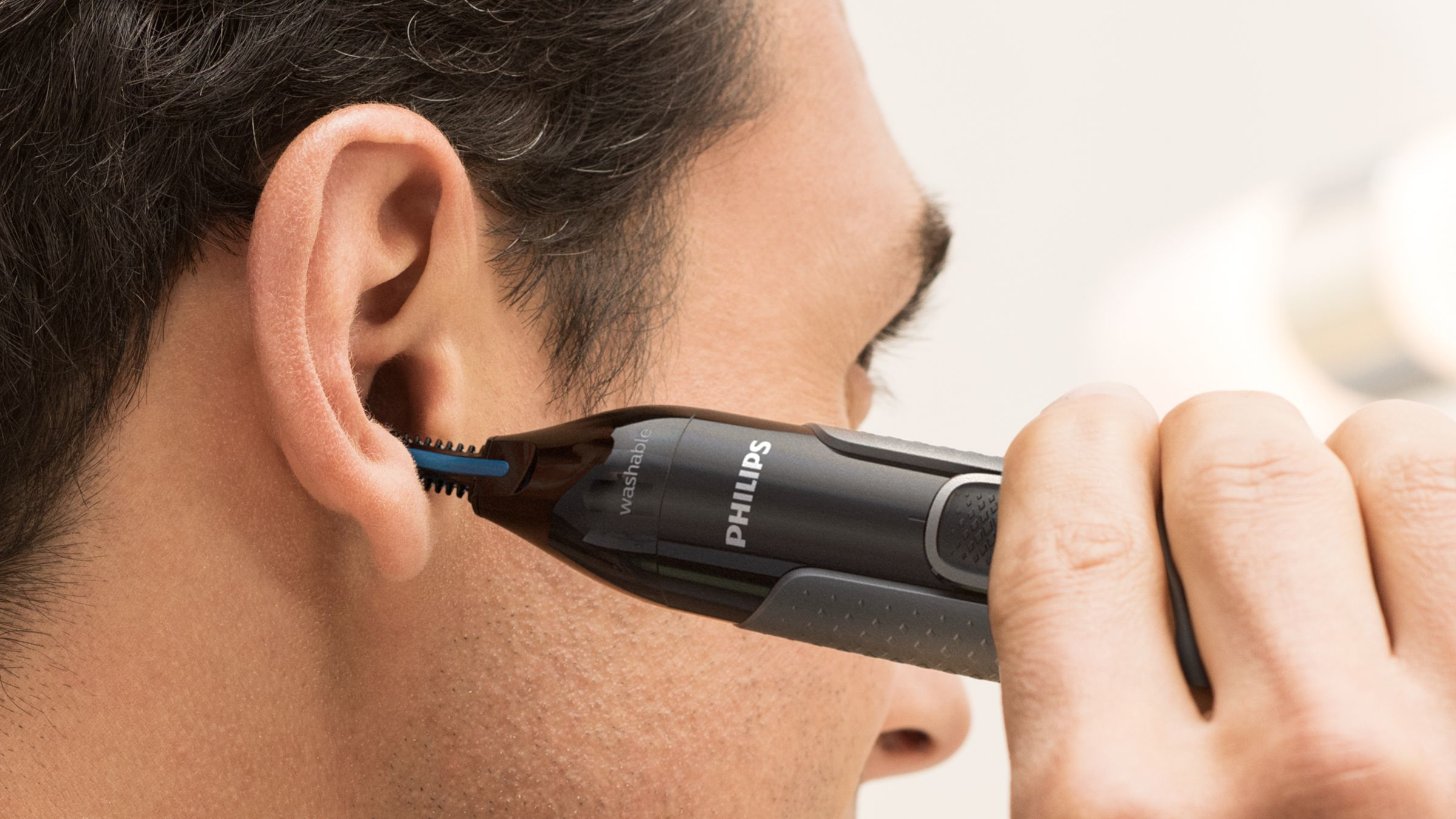 Een man die oorhaar trimt met een Philips trimmer. Close-up van oor en trimmer.
