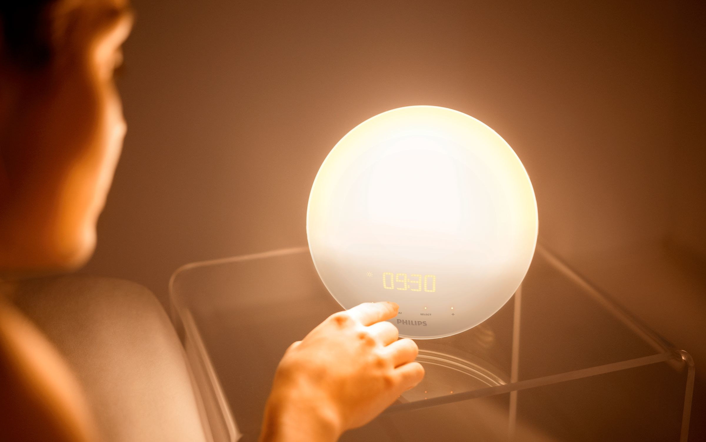 Une personne touche un réveil Philips blanc avec une lueur vive.