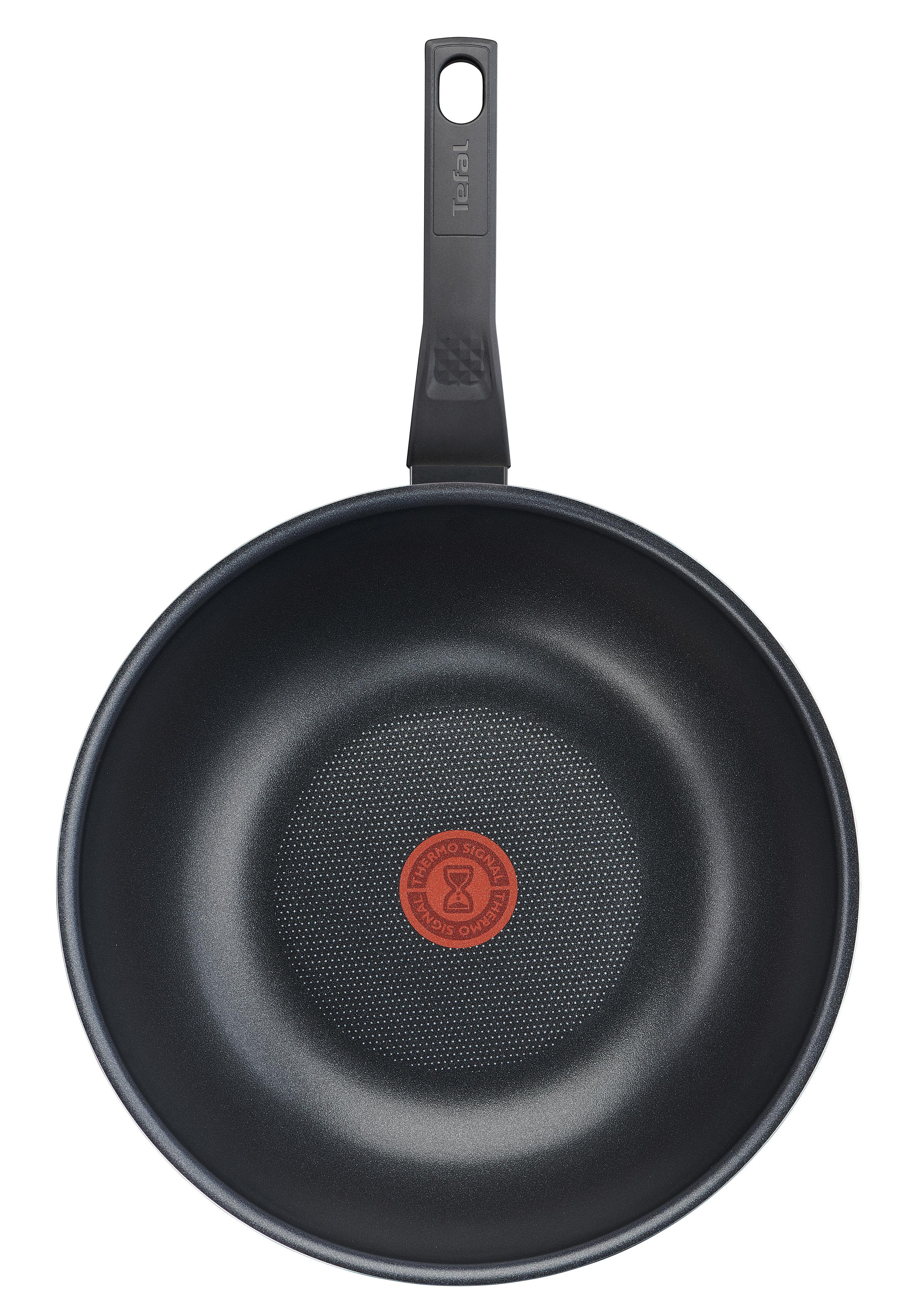 Draufsicht auf eine schwarze Tefal Wok-Pfanne mit rotem Punkt, auf weißer Oberfläche.