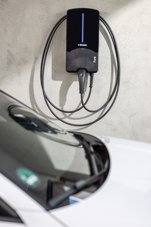 Eine schwarze Ladestation an einer Betonwand, darunter ein Auto sichtbar.