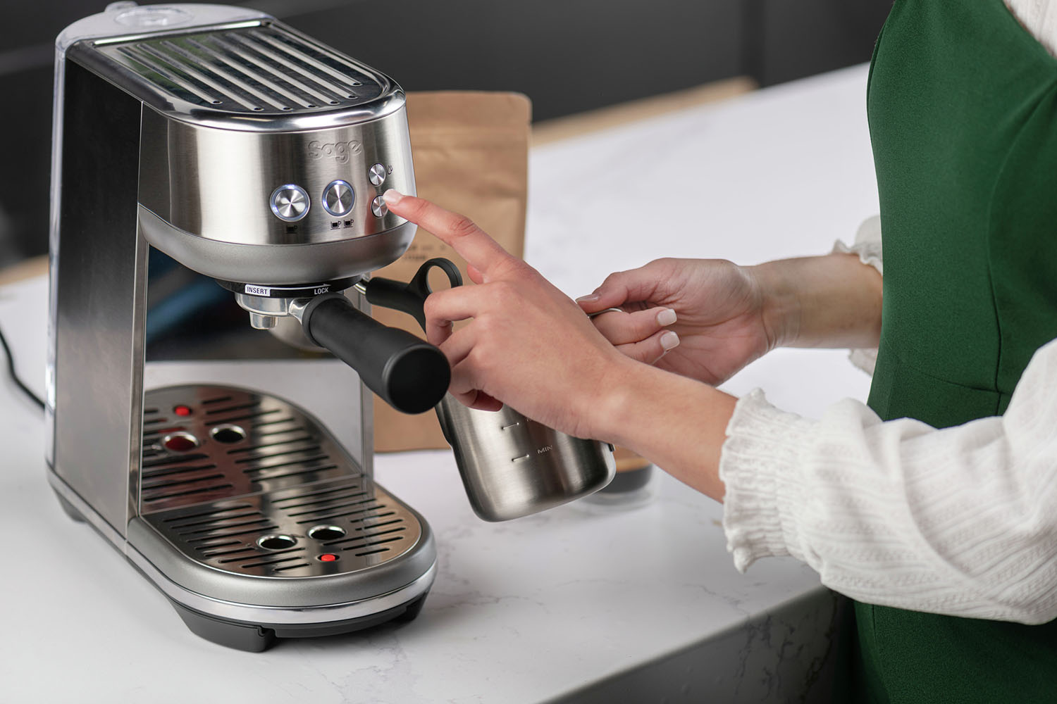 A person's hand presses a button on a silver espresso machine.