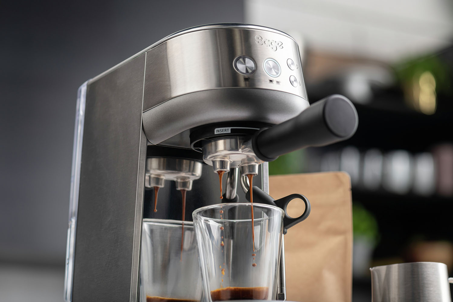 Silver espresso machine pouring coffee into two glasses. Brown liquid flows out.