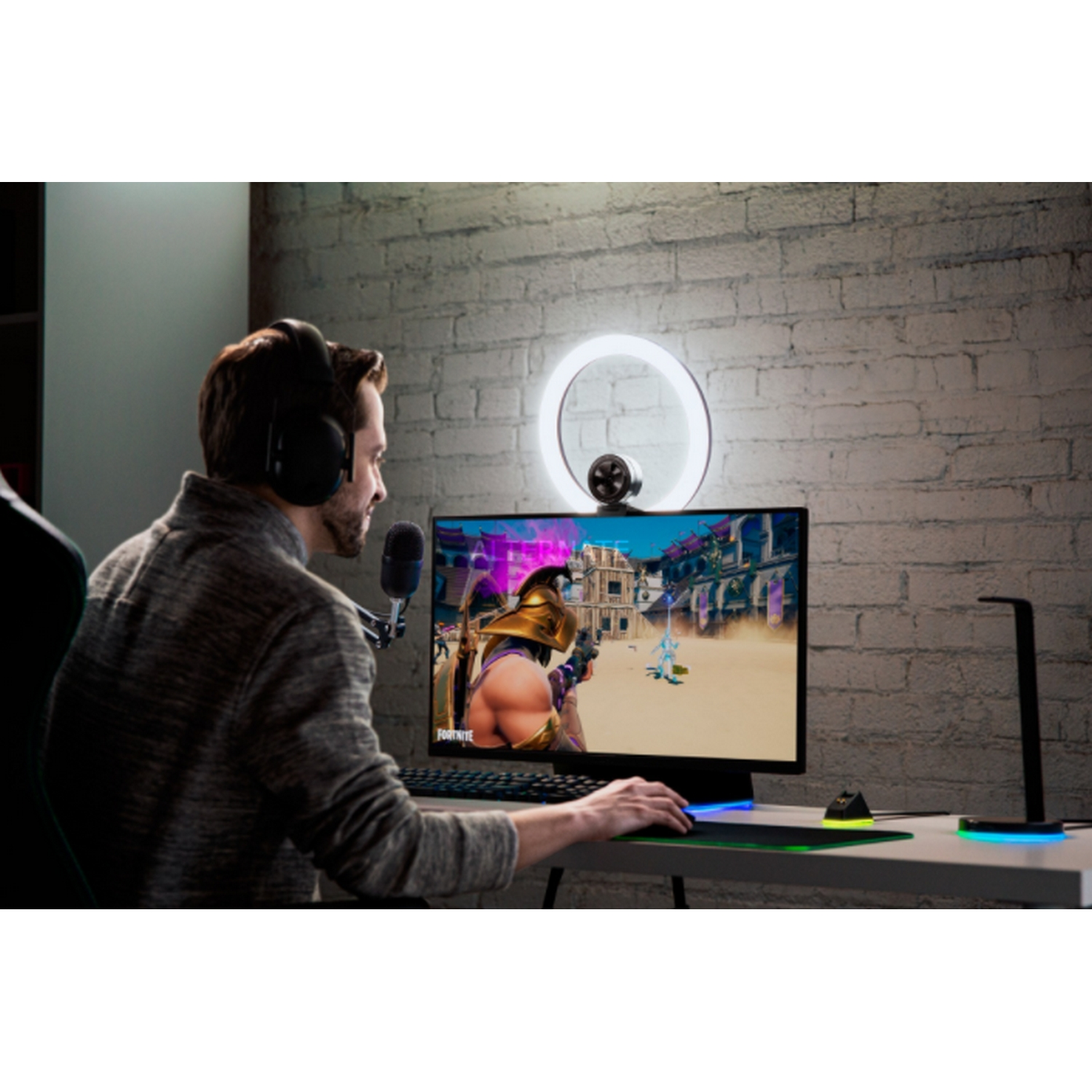 Hombre jugando con auriculares, micrófono y aro de luz. El monitor muestra un juego.