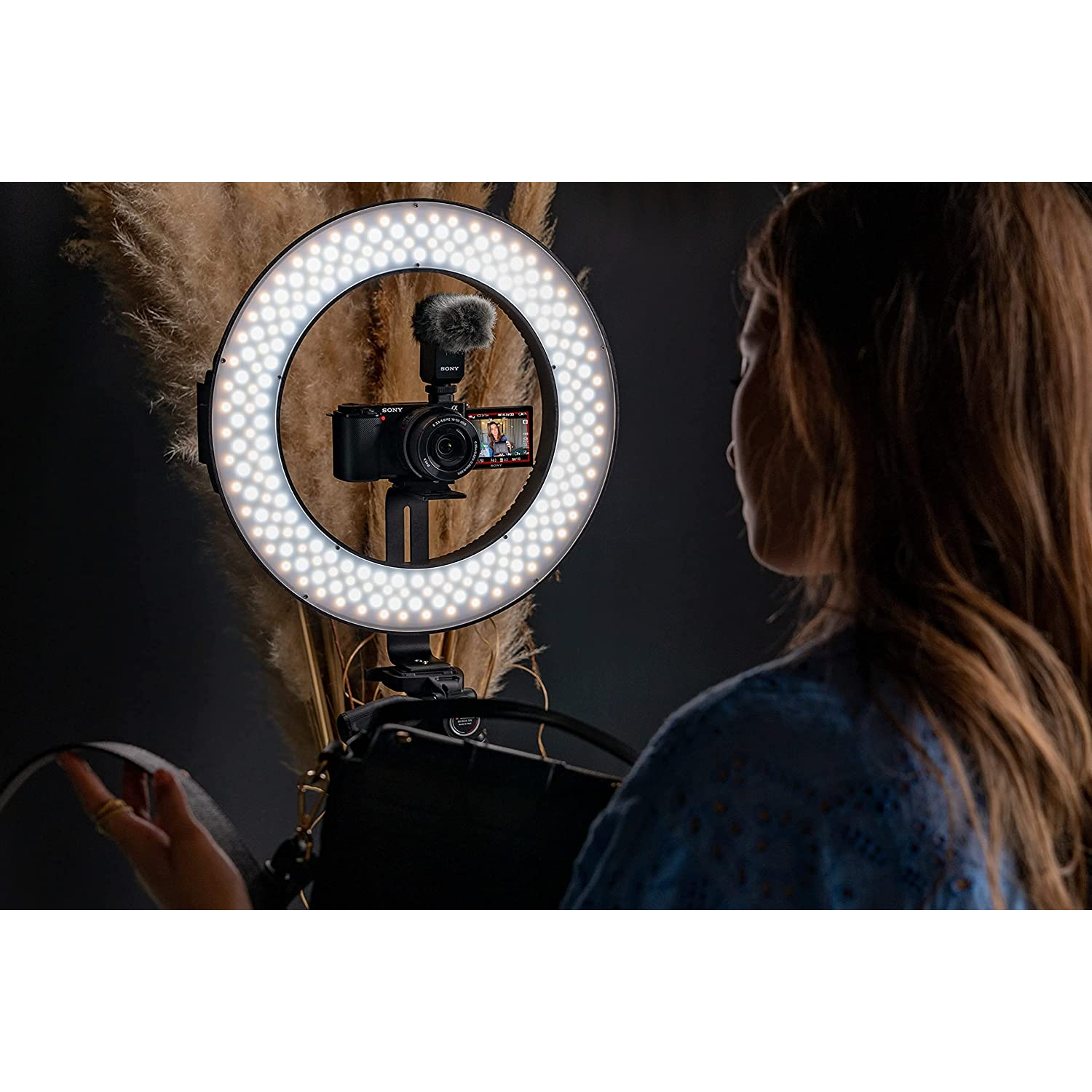 Mujer filmando con cámara y aro de luz. Hierba de la pampa marrón al fondo.