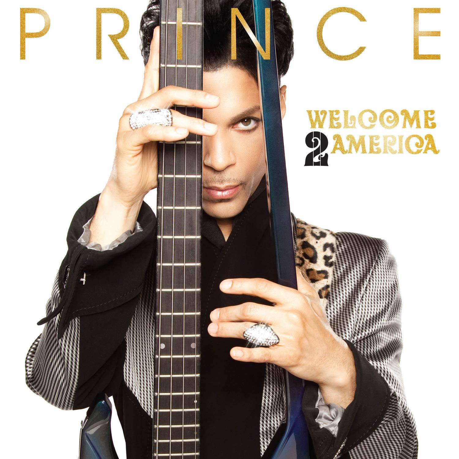 Prince hält eine Gitarre, das Cover seines Albums "Welcome 2 America". Er trägt Ringe.