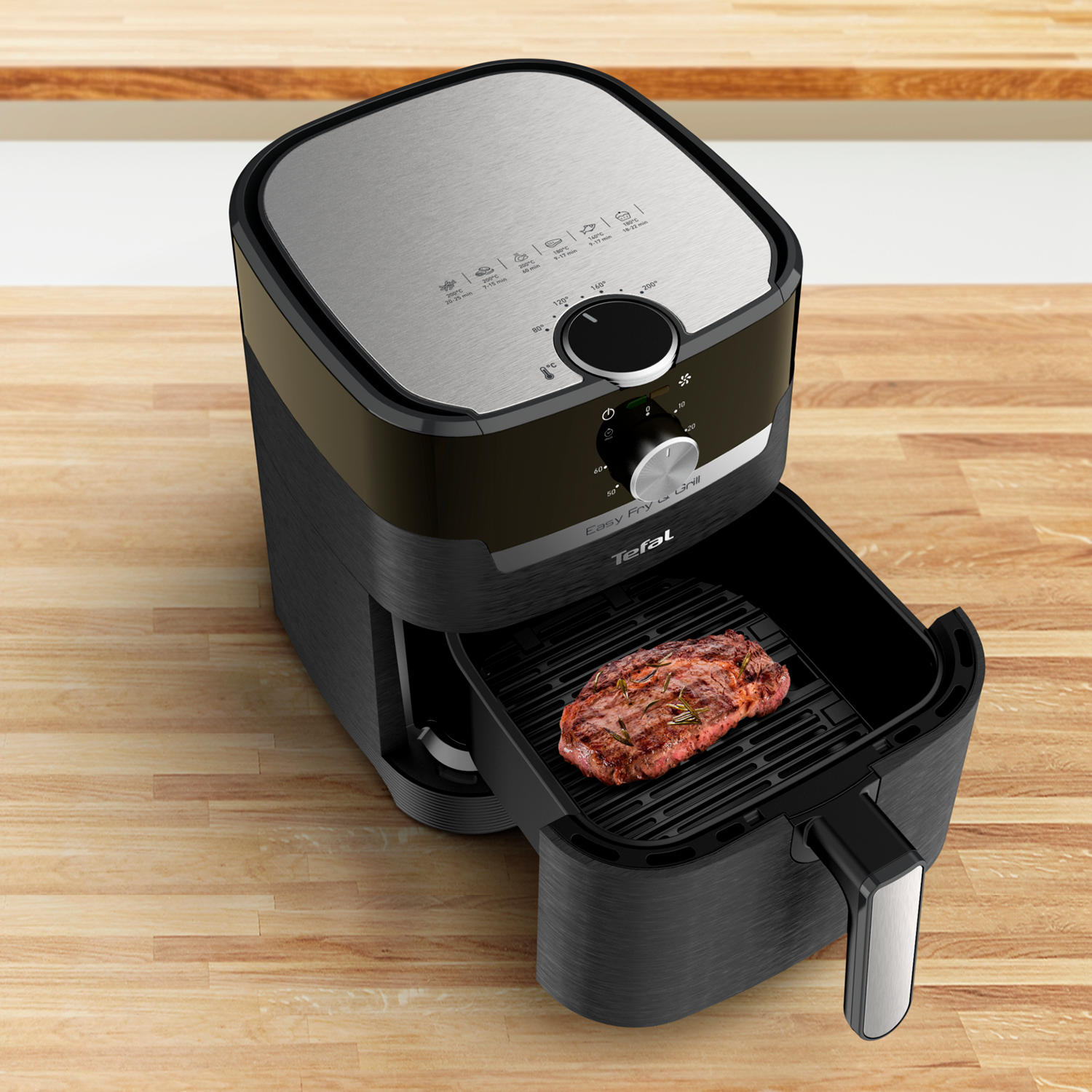 Zwarte en zilveren airfryer met biefstuk in de lade, op houten oppervlak. Knoppen en display.