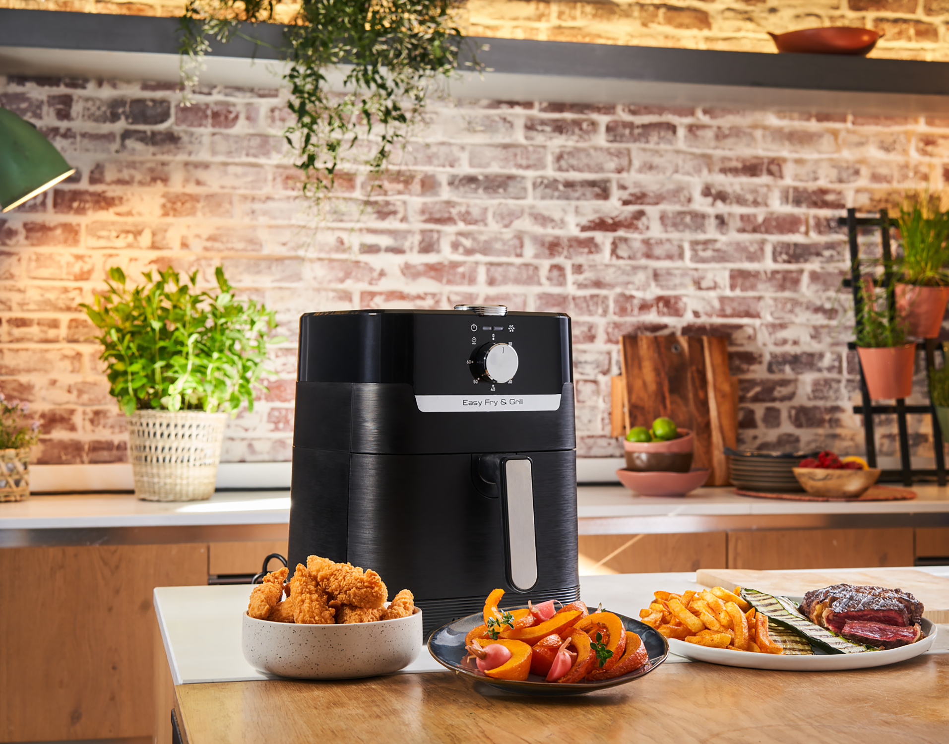 Zwarte airfryer met eten op het aanrecht. Gebakken kip, friet en groenten op tafel.