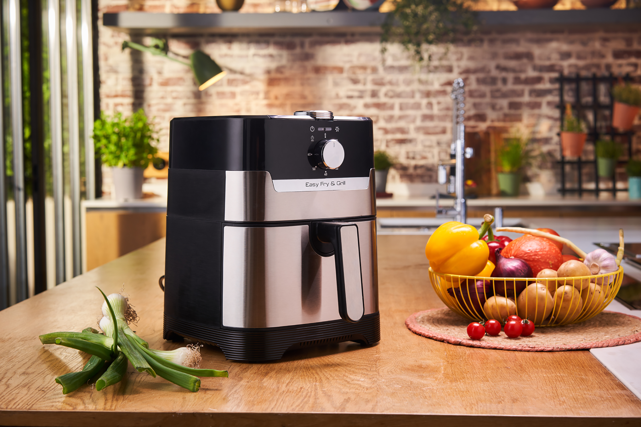 Black and silver air fryer on a wooden countertop. Basket of vegetables. Modern kitchen background.