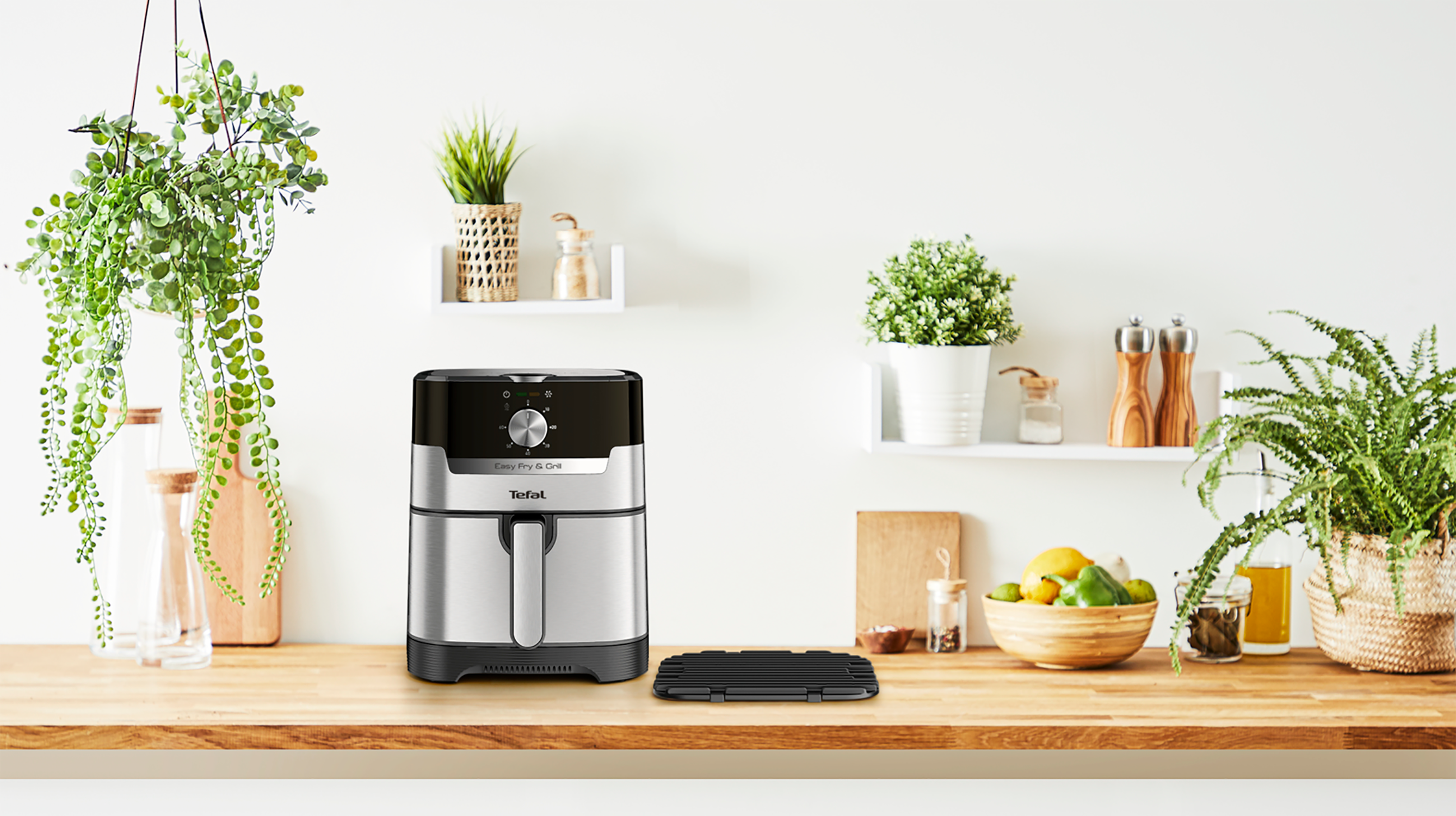 An air fryer on a wooden counter with plants and accessories in a kitchen.