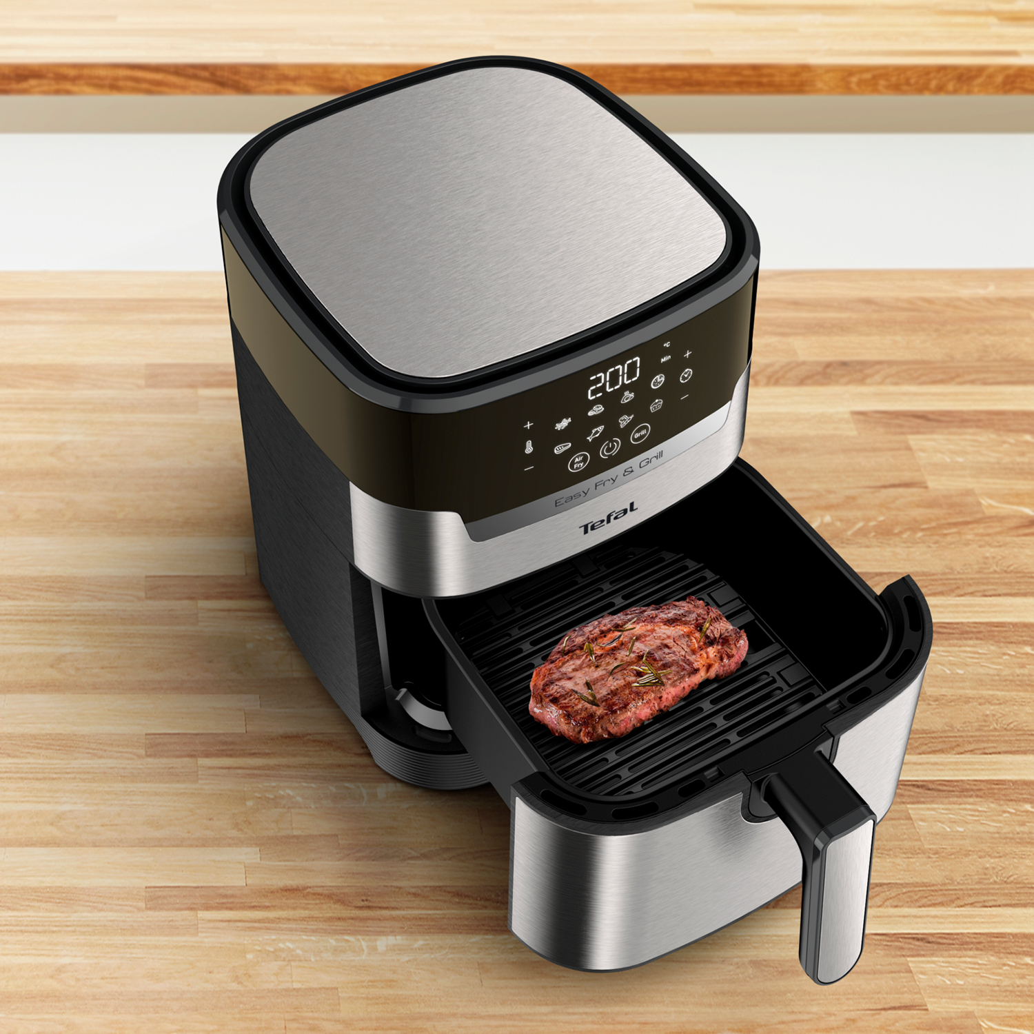 A Tefal air fryer with a steak inside, on a wooden surface. The top is metal.