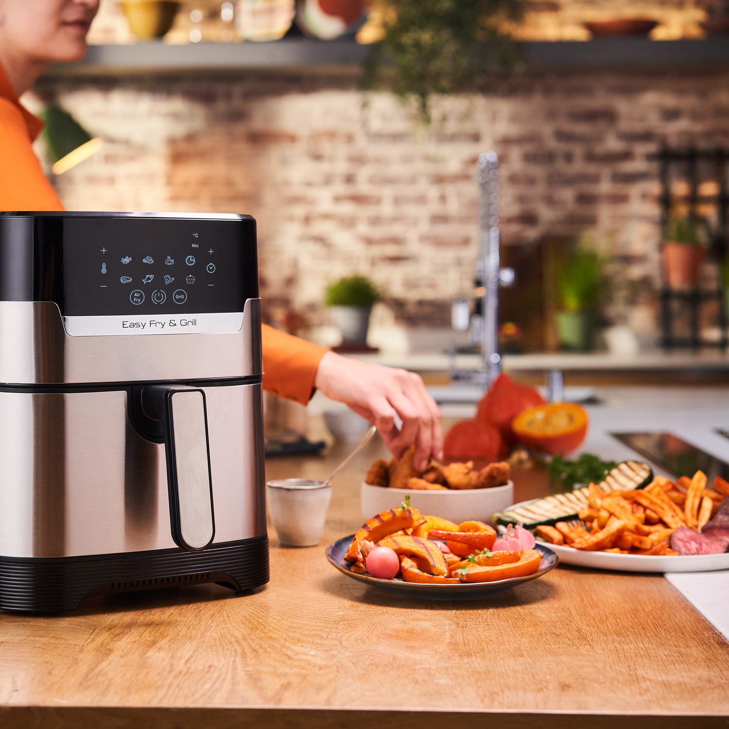 Air fryer, person, food on plates. Kitchen with brick wall.