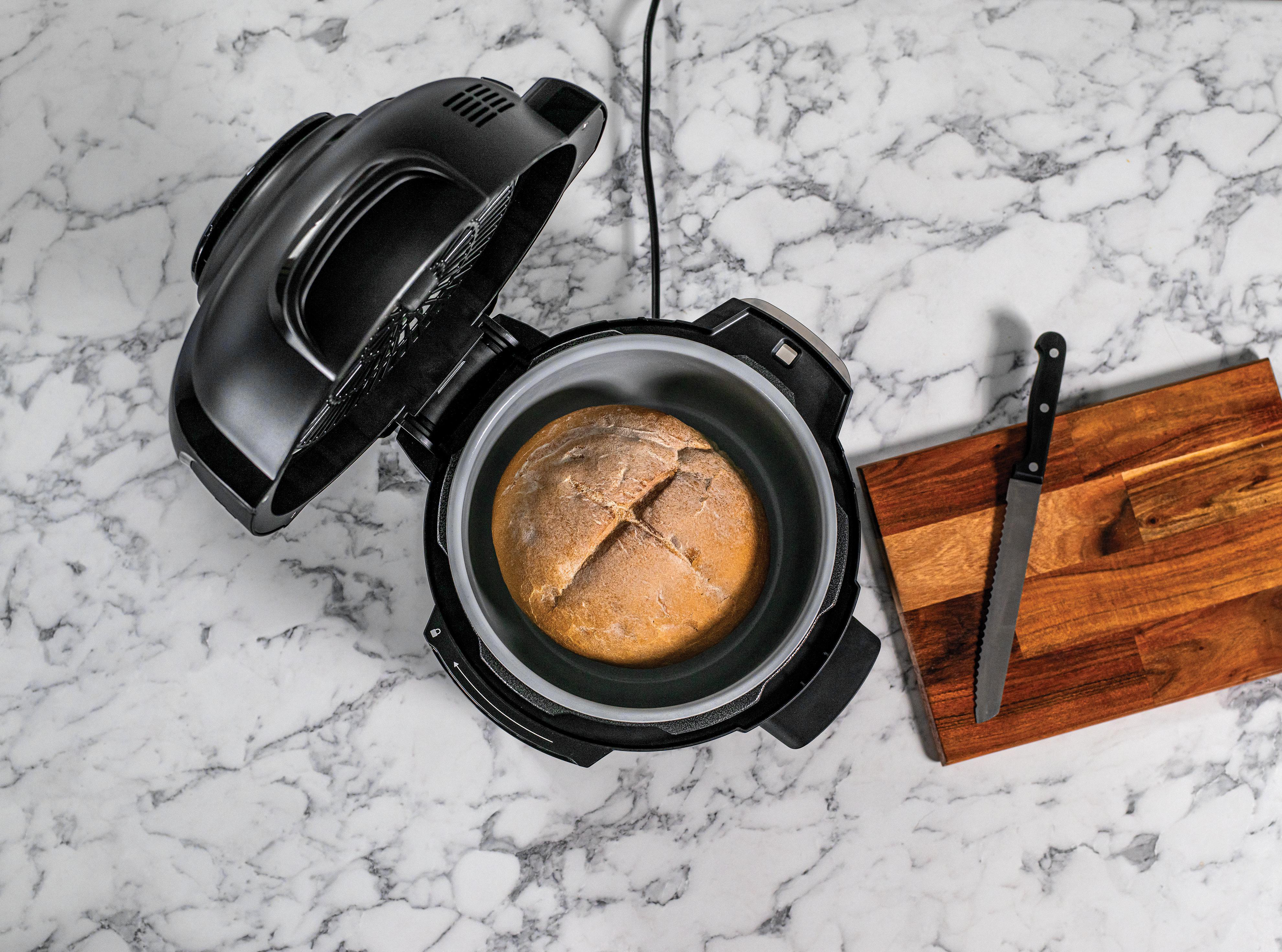Brot in einem schwarzen Airfryer, mit offenem Deckel und Messer auf einer Marmor-Arbeitsplatte.