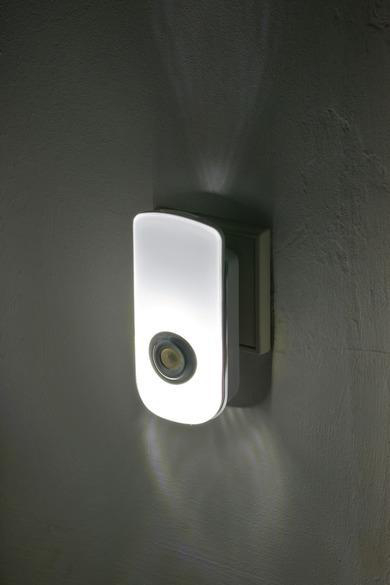 Ein weißes Nachtlicht, das in eine Steckdose gesteckt ist. Das Licht ist an und beleuchtet die Wand.