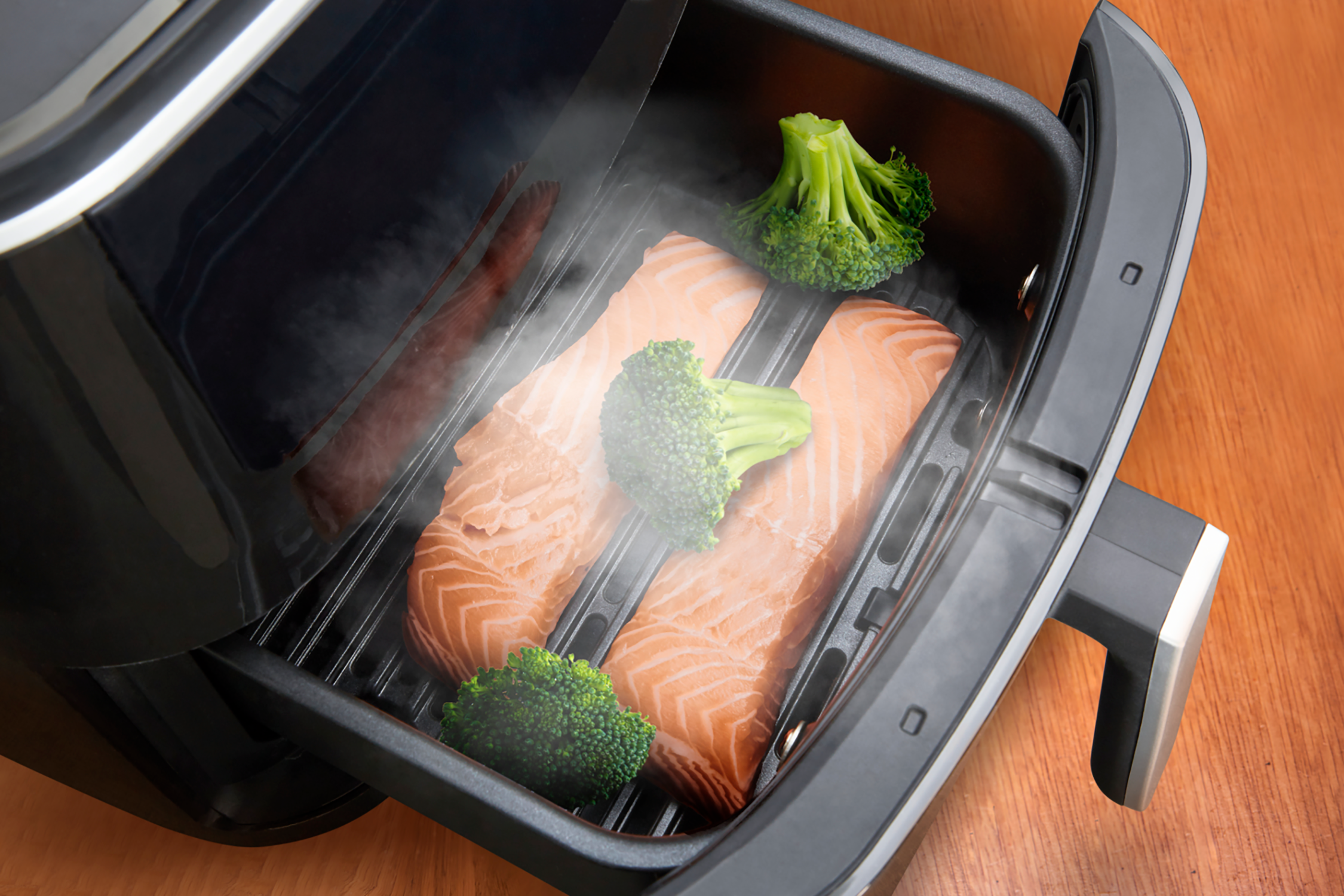 Zalmofilets en broccoliroosjes in een airfryer. Stoom is zichtbaar.