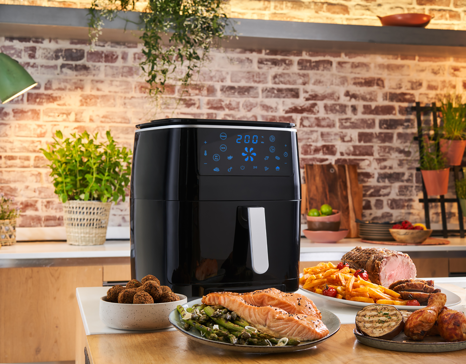 Een airfryer met gekookt voedsel zoals zalm, friet en kip op een tafel.