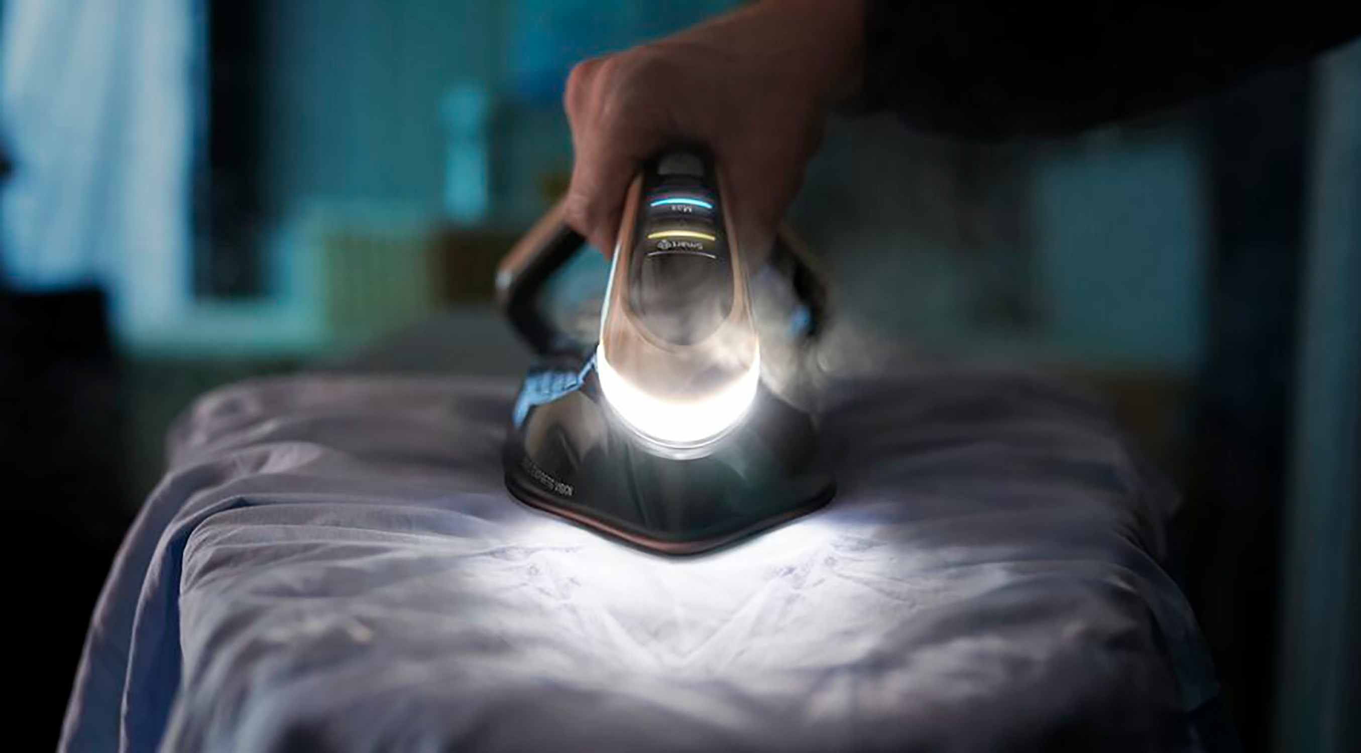 A person ironing a blue shirt with a steam iron. The iron is black and white.