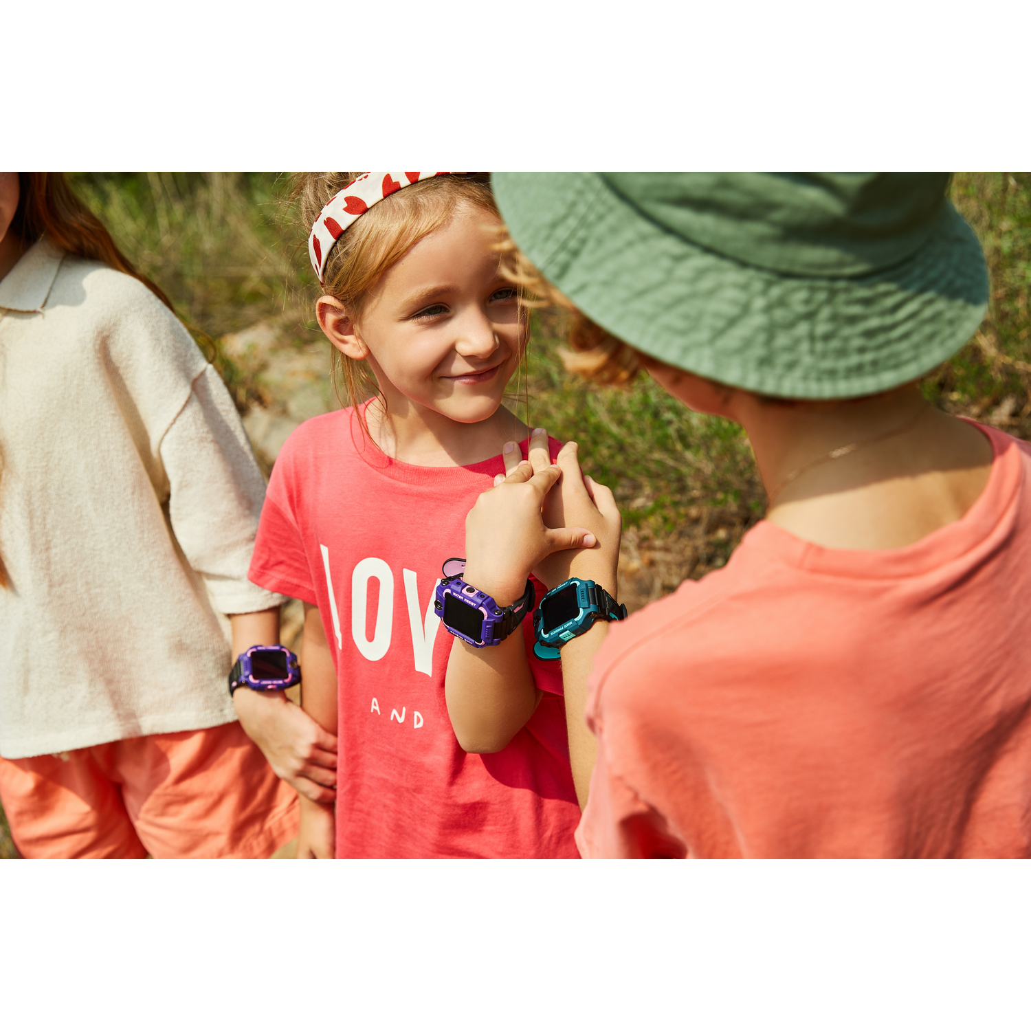 Niños usando smartwatches, sonriendo, con sombrero verde y diadema roja.