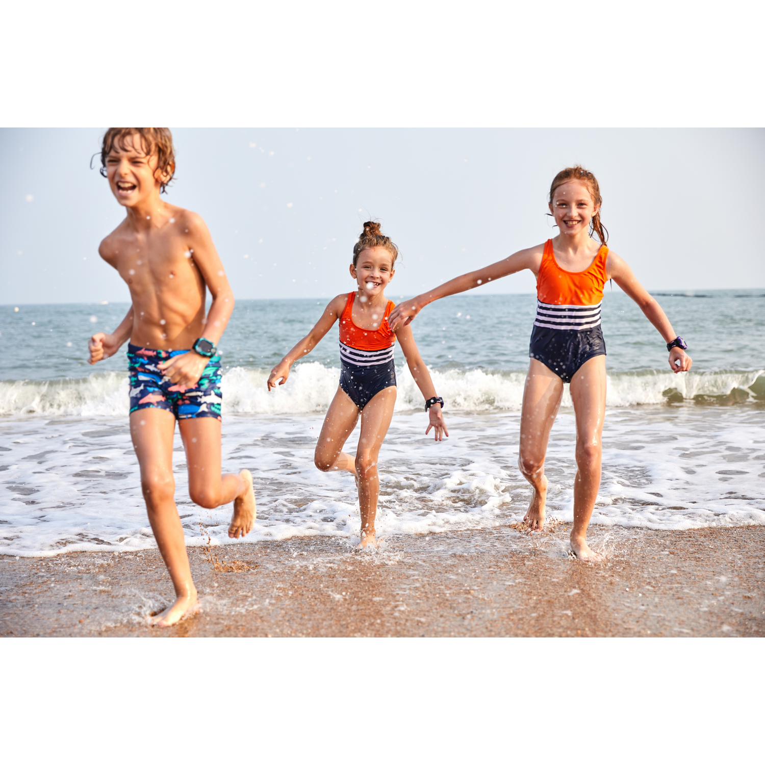 Tres niños corriendo en una playa hacia el agua, día soleado.