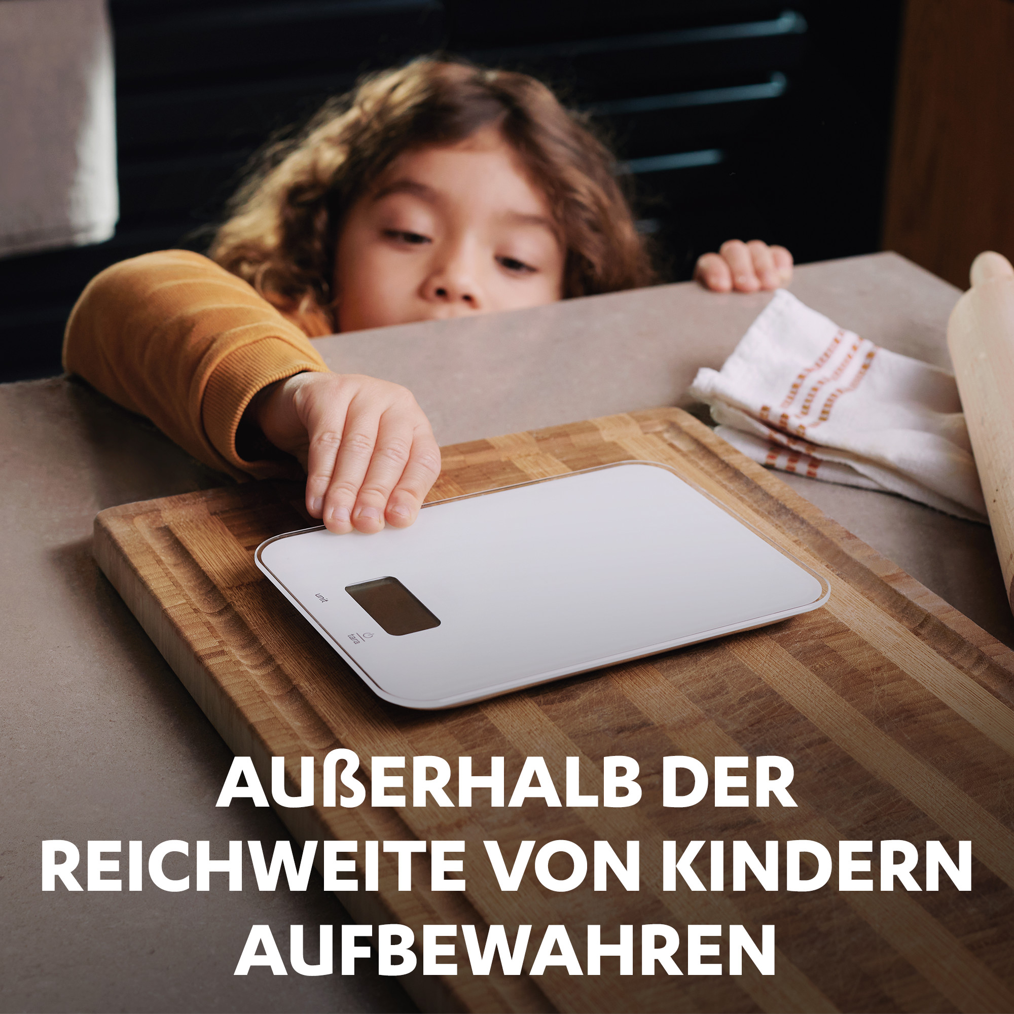 Ein Kind greift nach einer digitalen Waage auf einem Holzschneidebrett.