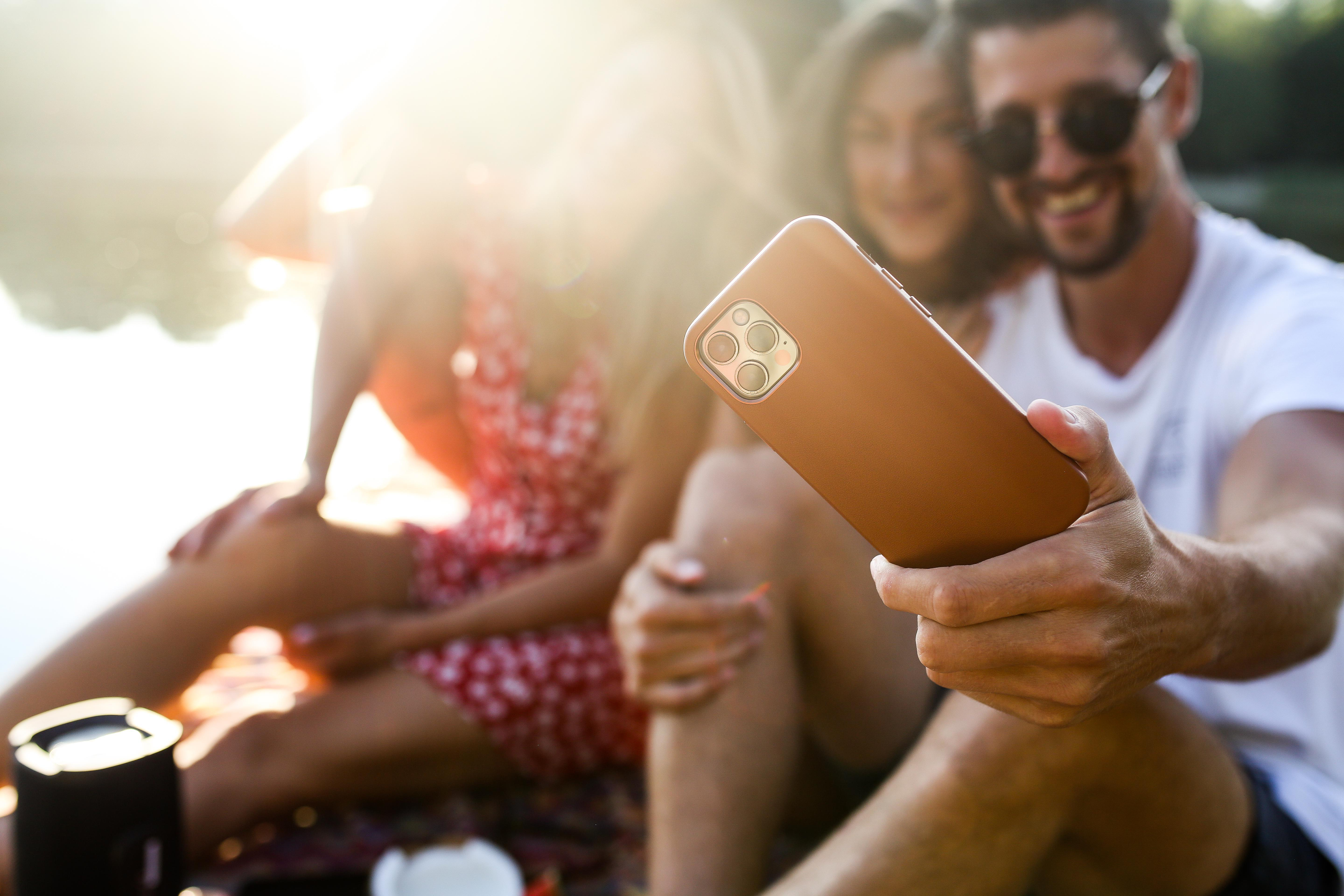 Drei Personen machen ein Selfie mit einem Telefon im Vordergrund im Freien.