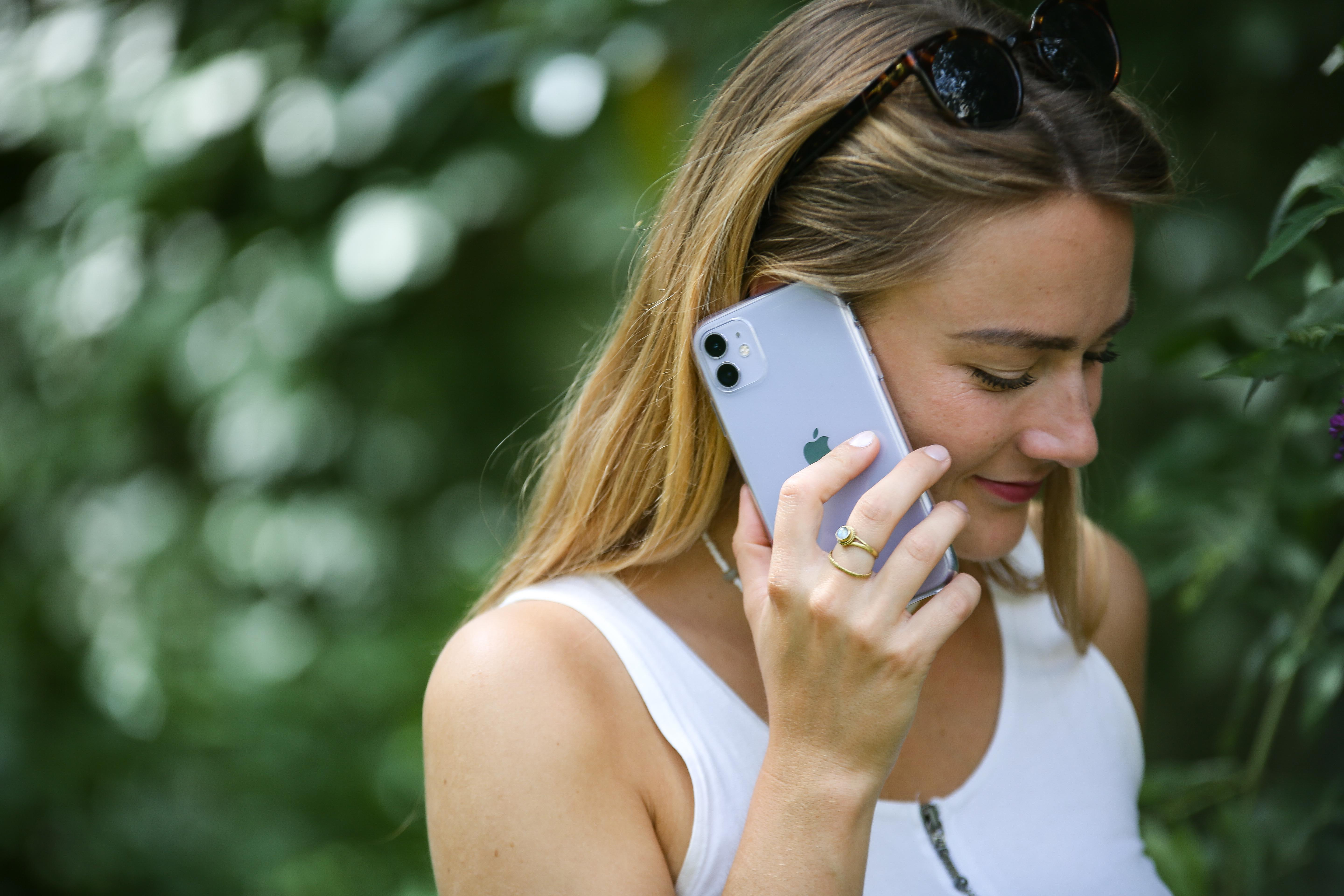 Frau telefoniert, lächelt, in einer Gartenumgebung.