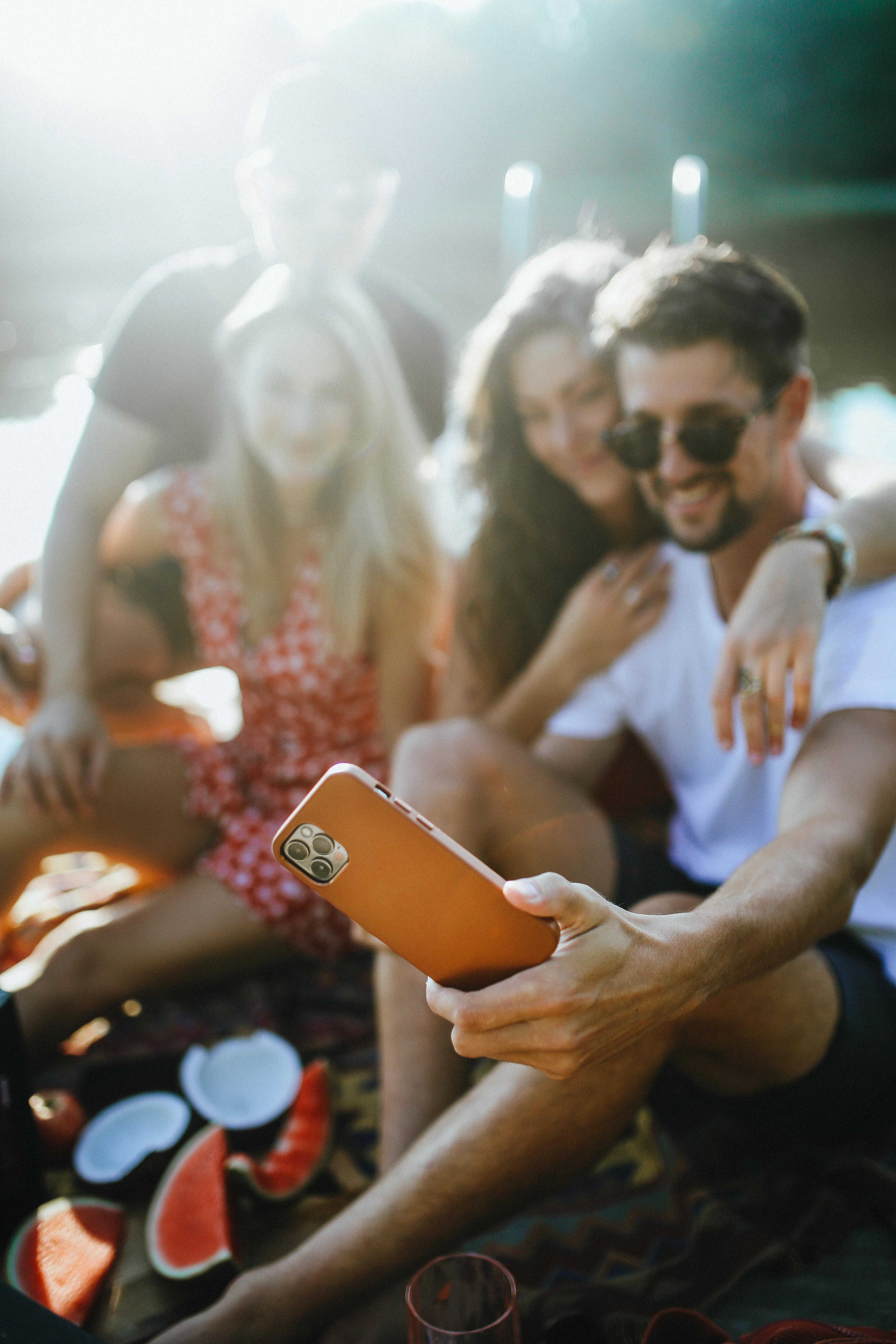 Gruppe von Leuten, die ein Selfie mit einem Telefon machen, Wassermelone und ein Glas auf dem Boden.