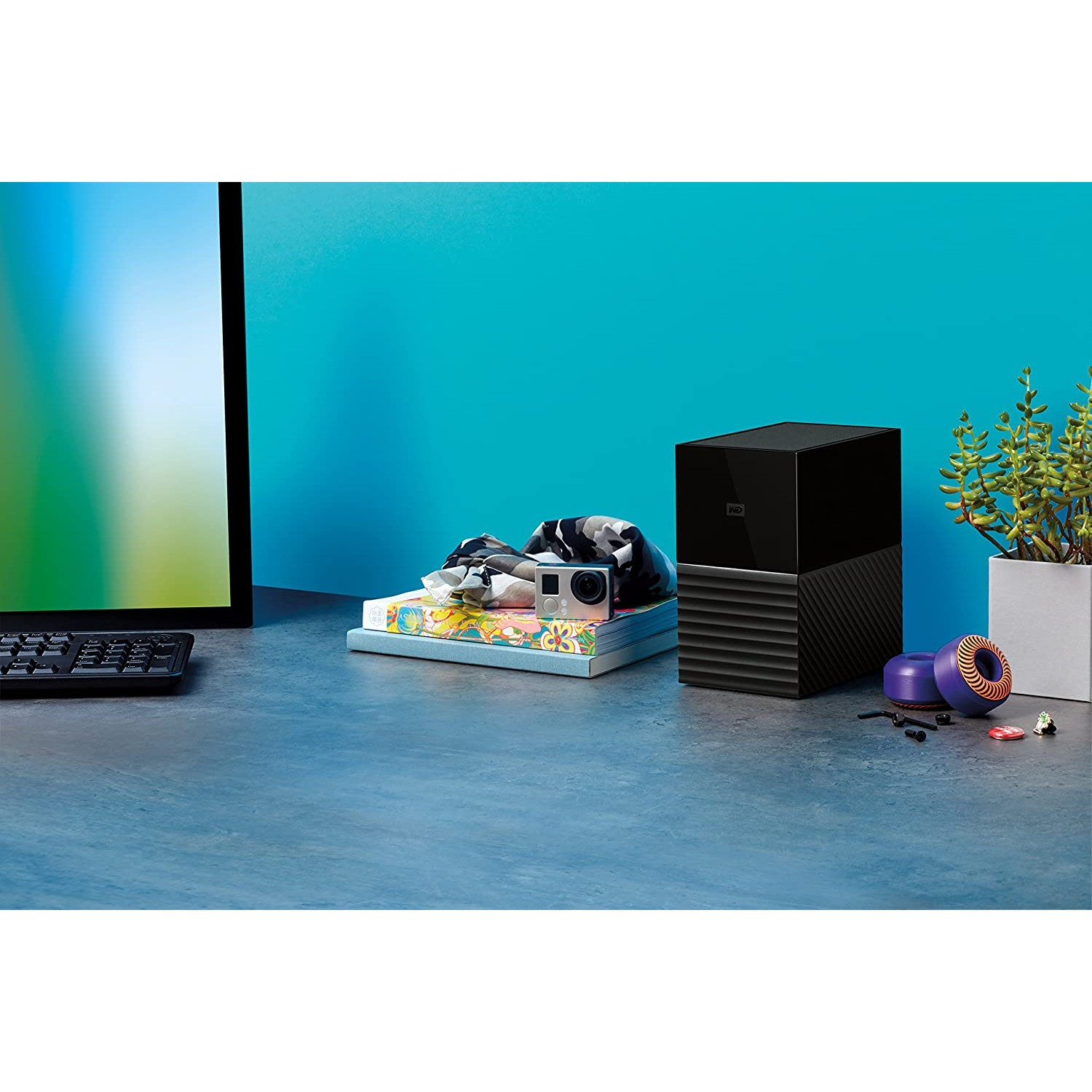 Escritorio con monitor, disco duro, cámara y otros objetos en una habitación.
