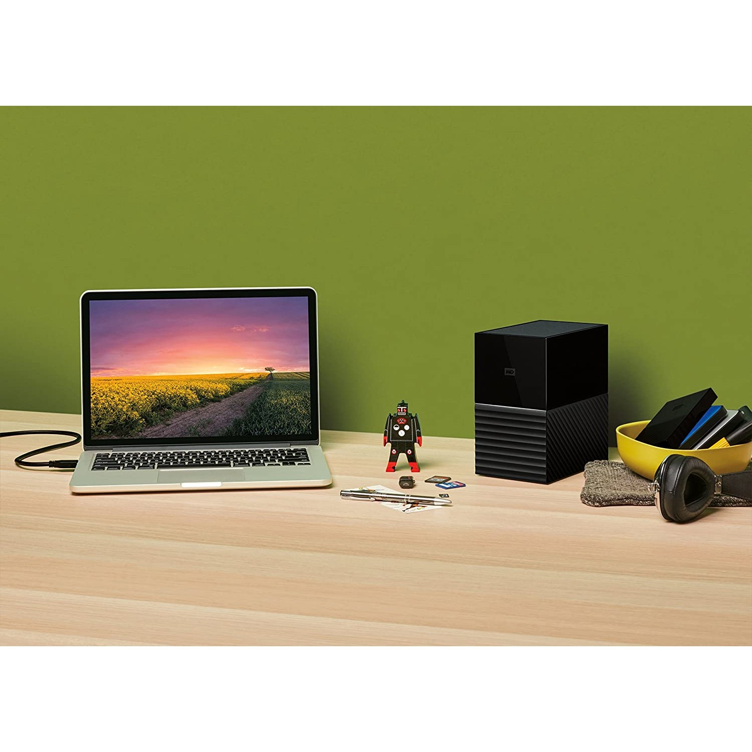 Laptop, juguete robot y disco duro externo en un escritorio de madera. Pared verde al fondo.