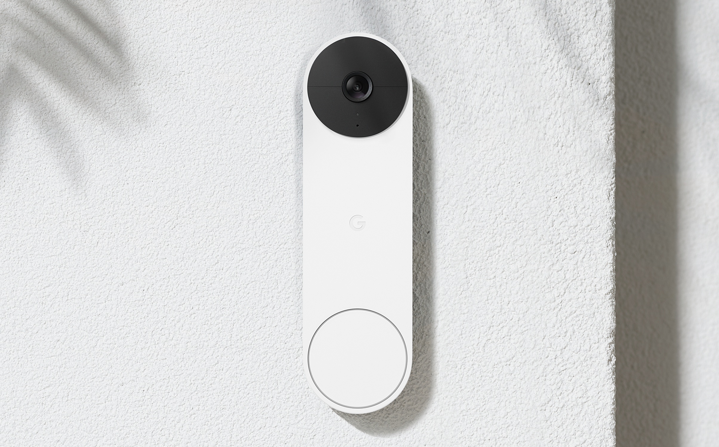 Witte slimme deurbel gemonteerd op een getextureerde muur, met een zwarte camera en een knop.