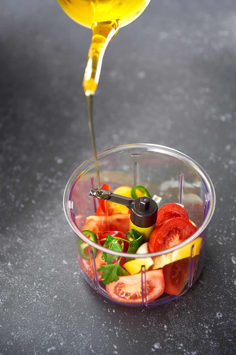 Olive oil being poured into a transparent container holding chopped vegetables.
