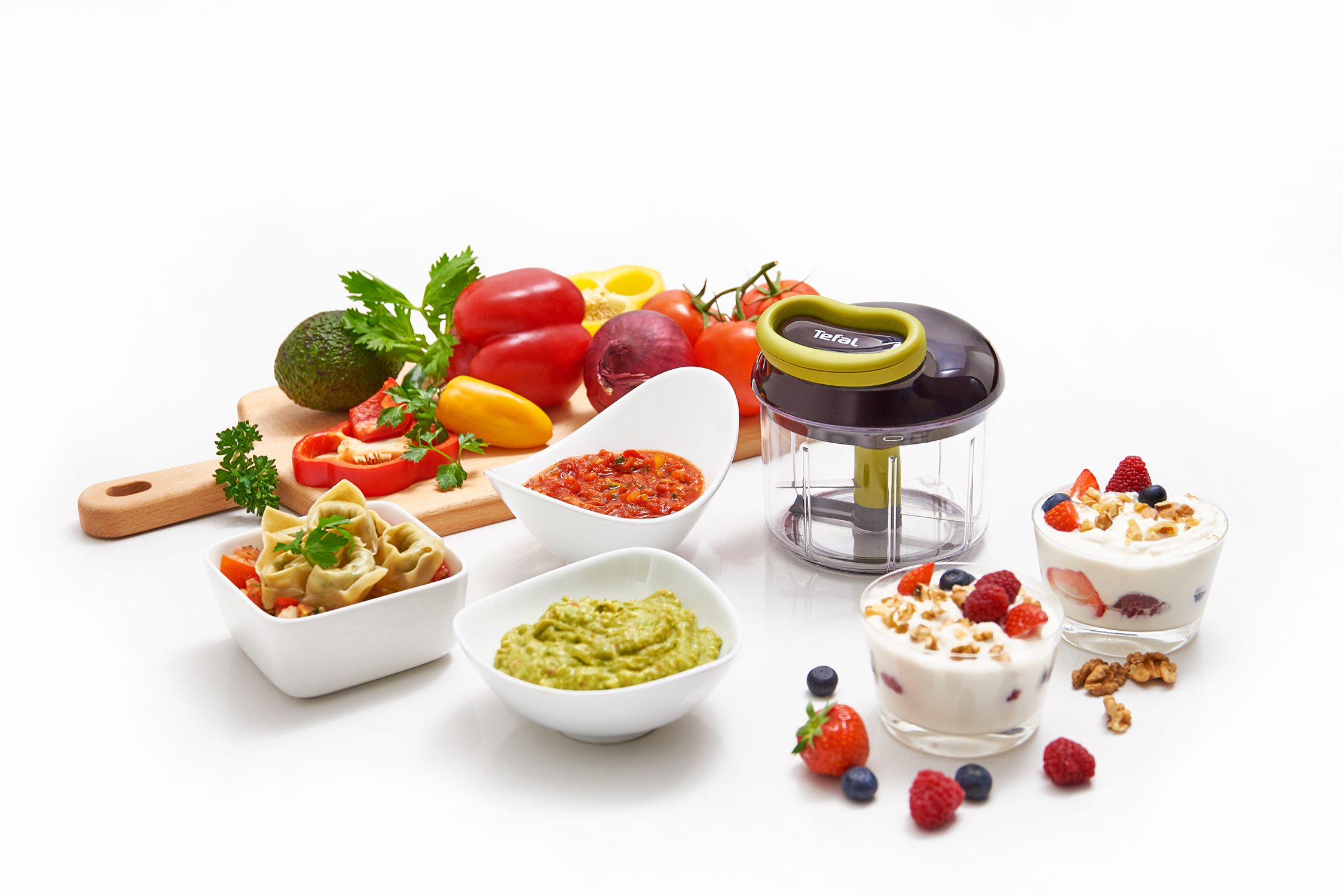 A Tefal food chopper with ingredients: vegetables, dips, and yogurt parfaits, all on a white surface.