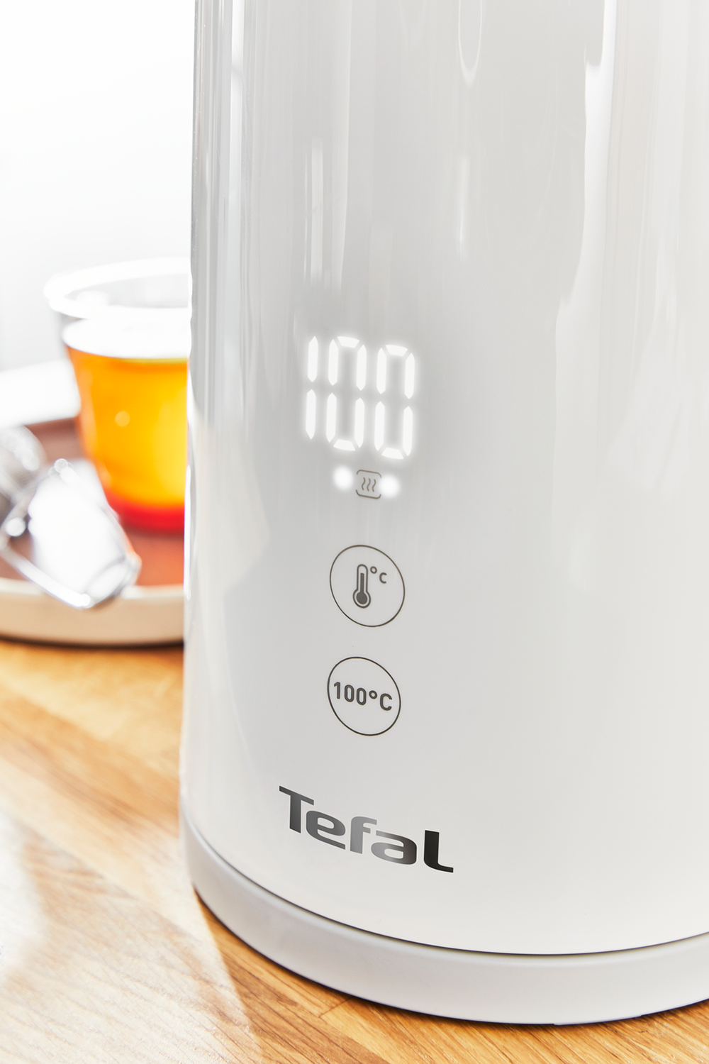 Witte Tefal waterkoker met digitaal display. Het display toont de temperatuur. Houten tafel.