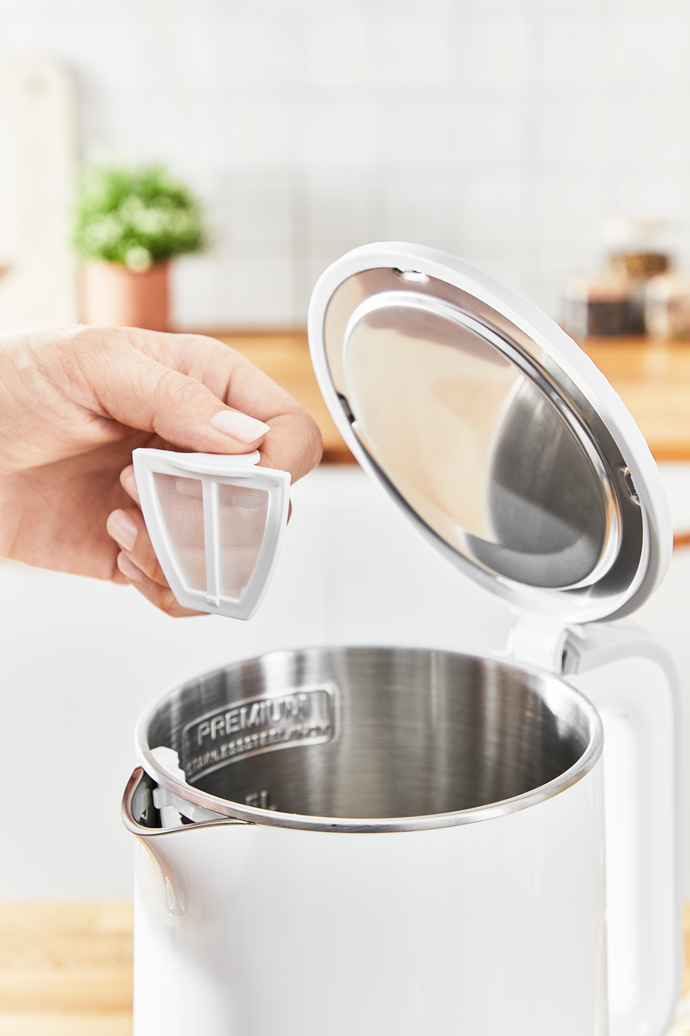 Een hand houdt een filter uit een witte waterkoker vast, waarbij de binnenkant van de waterkoker zichtbaar is.