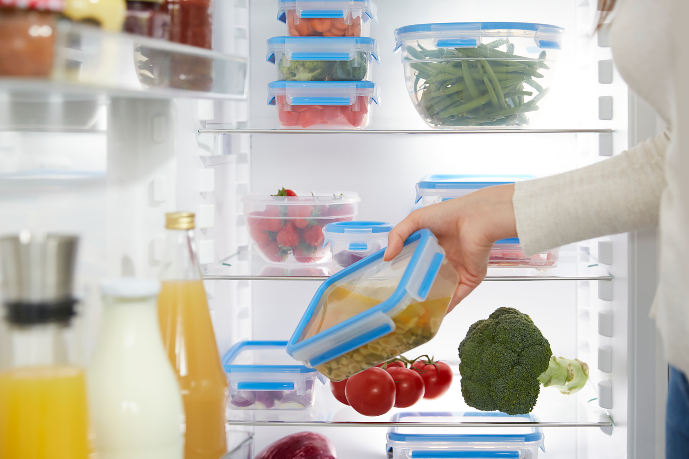 Woman reaching into a refrigerator filled with food containers and vegetables.