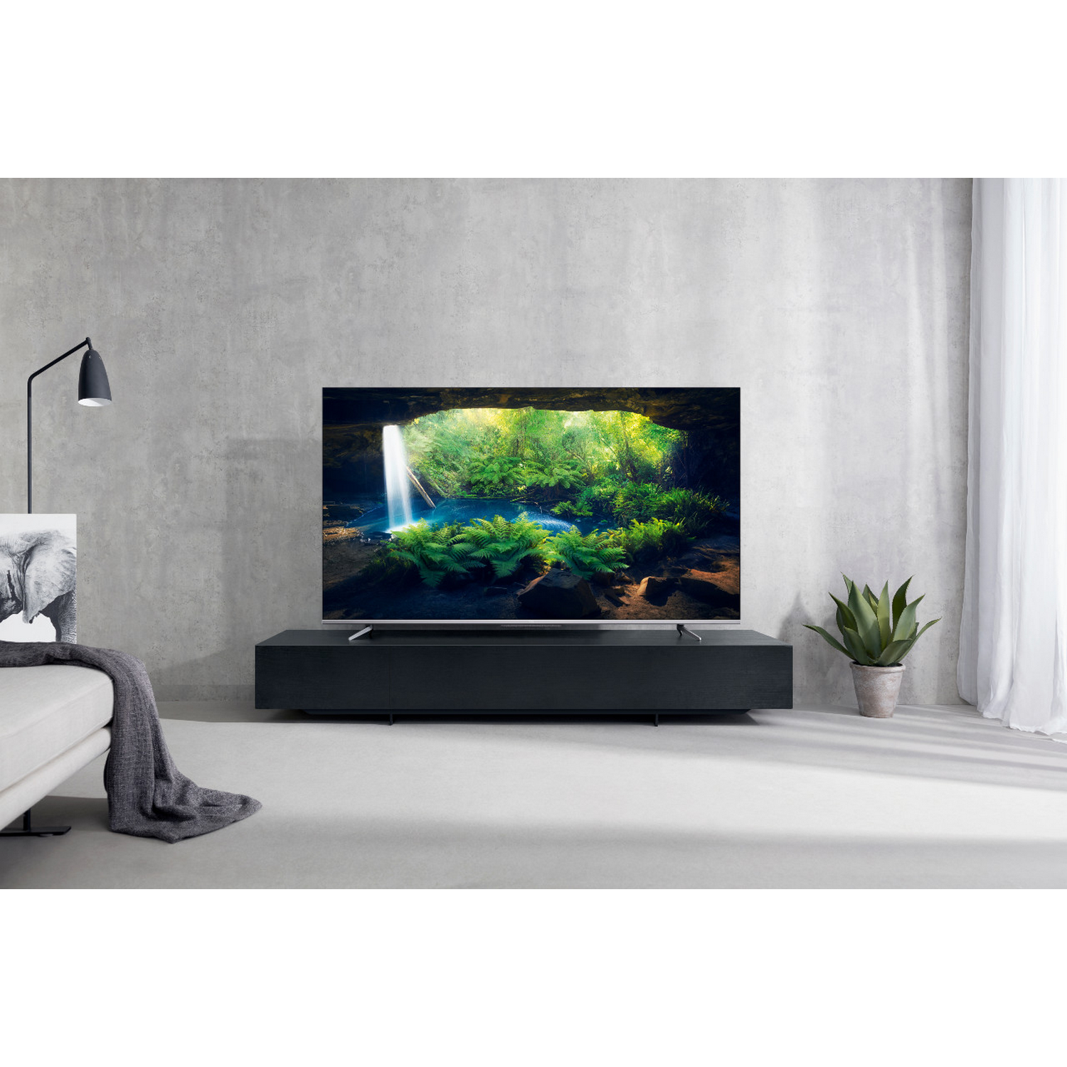 Gran televisor en un soporte negro muestra escena de cascada. Cortina blanca a la derecha.
