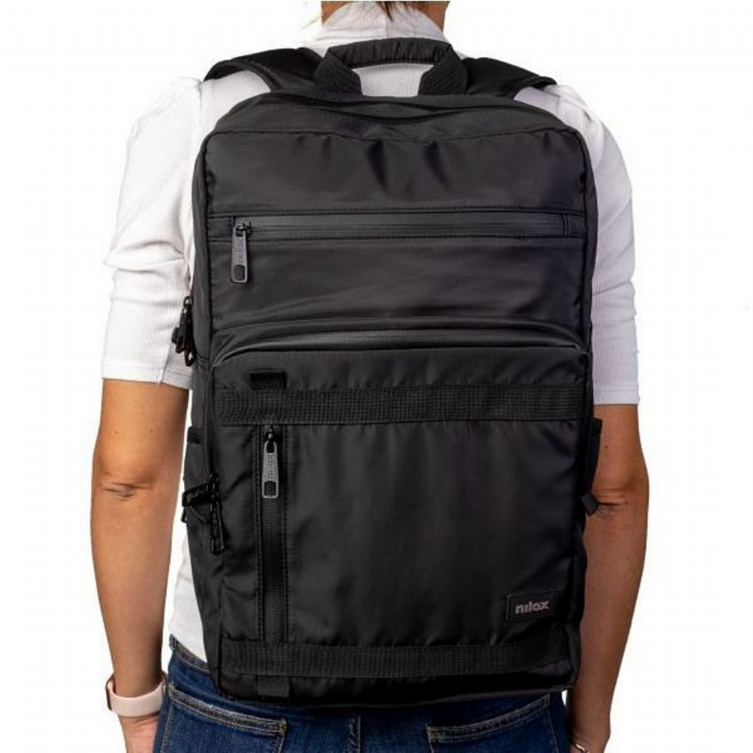 Persona con mochila negra, vista trasera. Correas y cremalleras visibles.