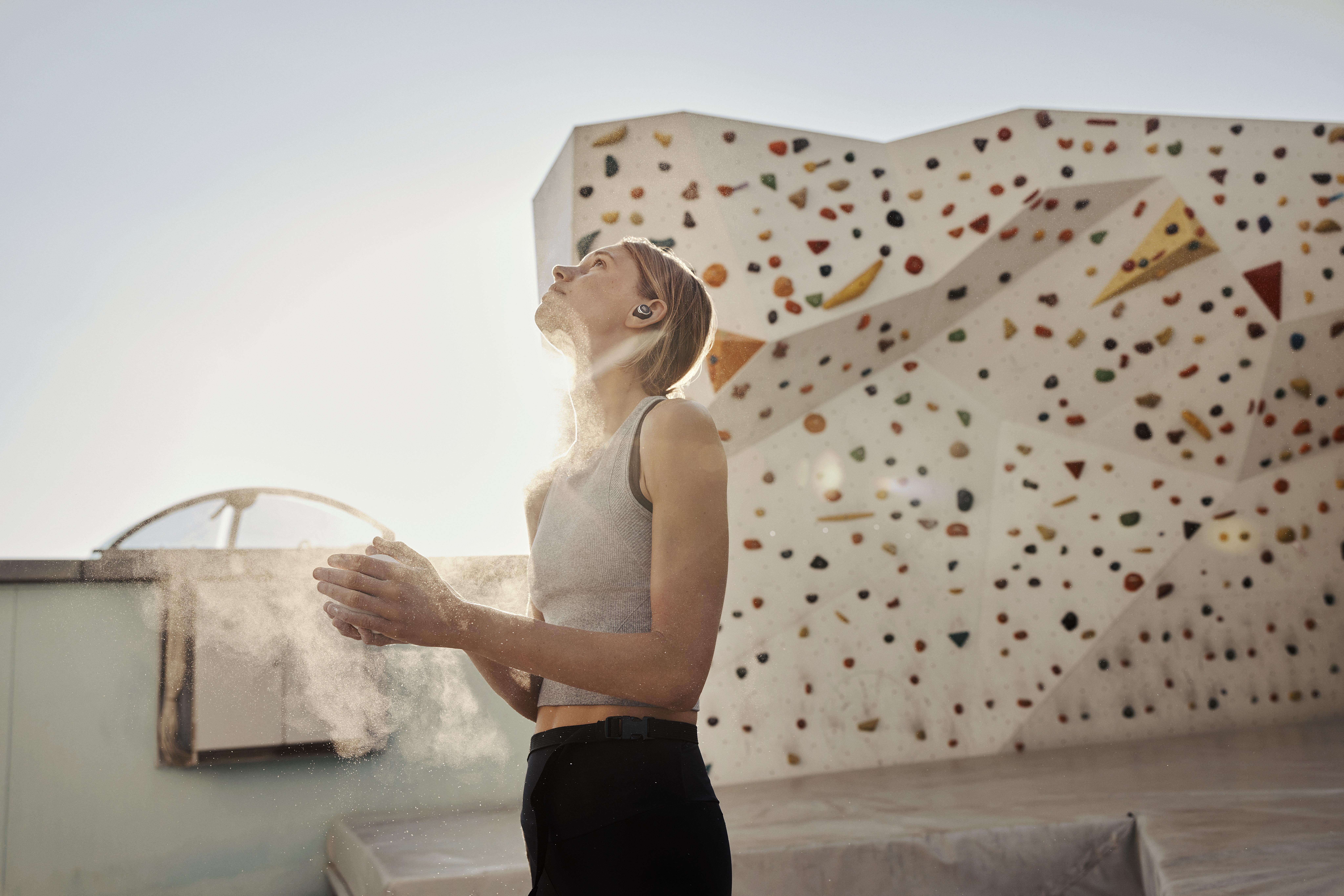 Eine Frau klettert und klatscht in die Hände, mit Kreide bedeckt, vor einer Kletterwand.
