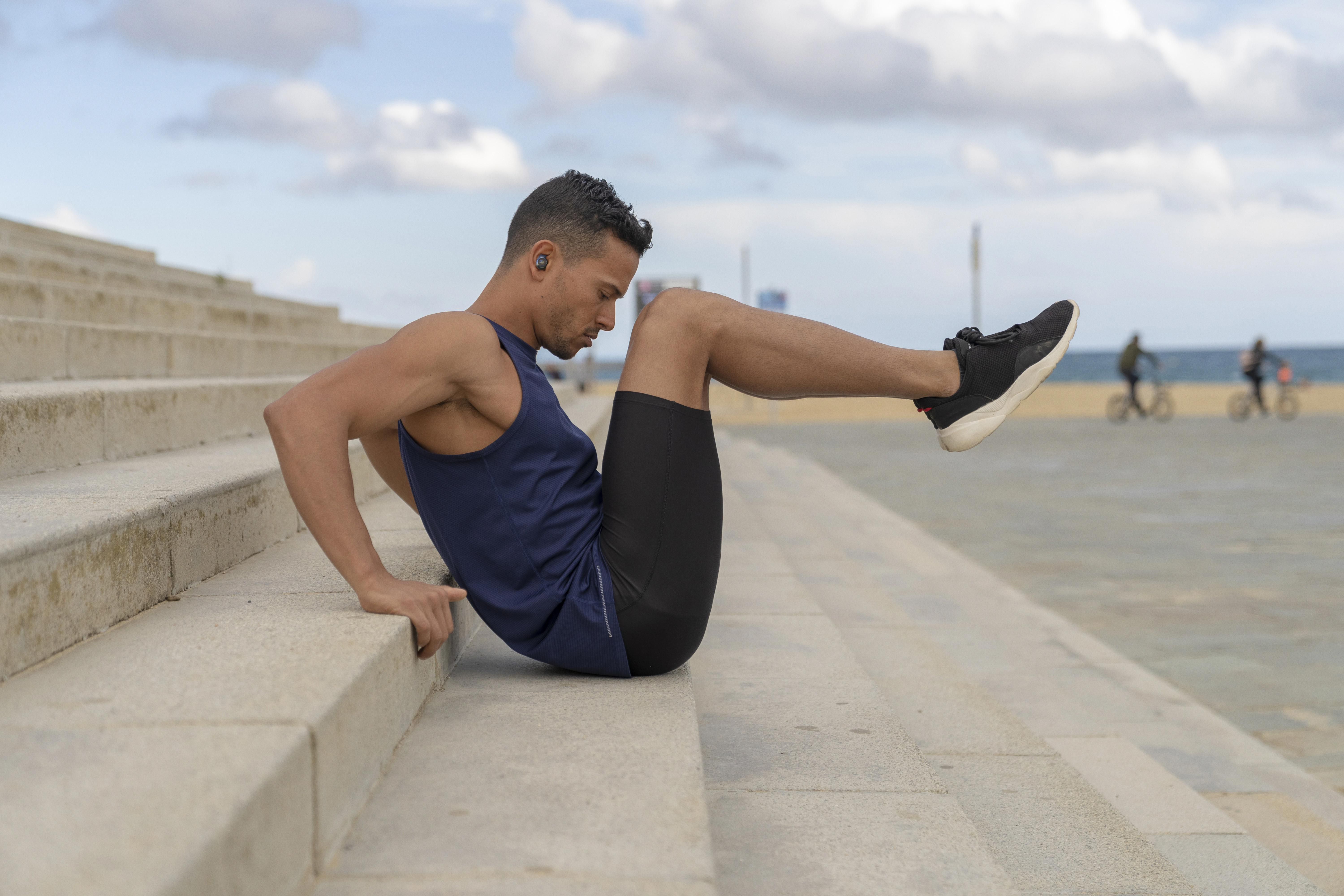 Mann trainiert auf Treppen am Strand, macht Sit-ups mit Ohrhörern.