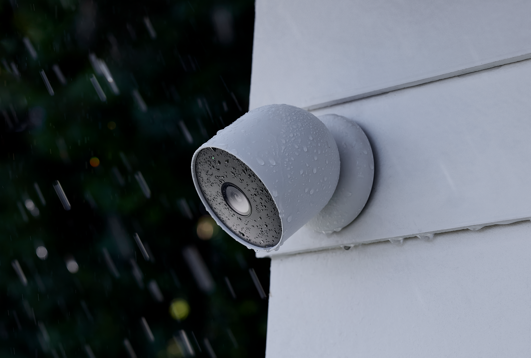 Witte beveiligingscamera op witte muur, met regen op de achtergrond.