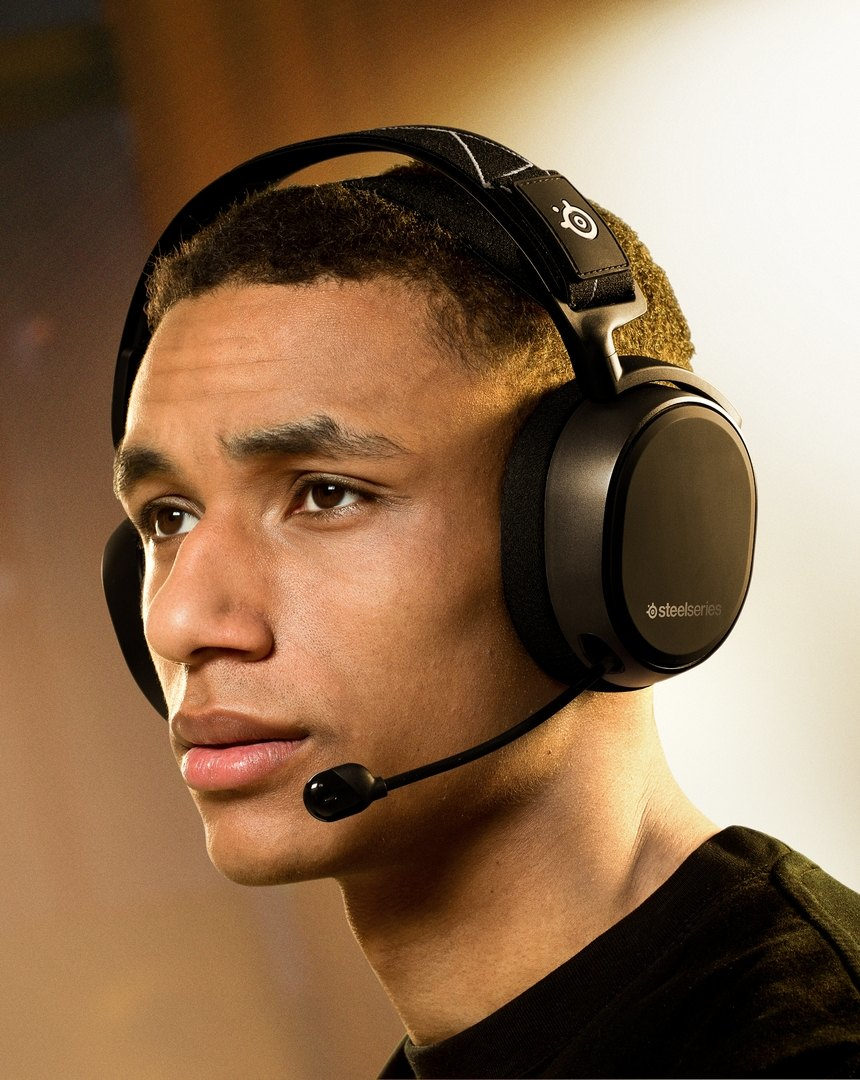 Egy fiatal fekete SteelSeries fejhallgatót visel, mikrofonnal, jobbra nézve.