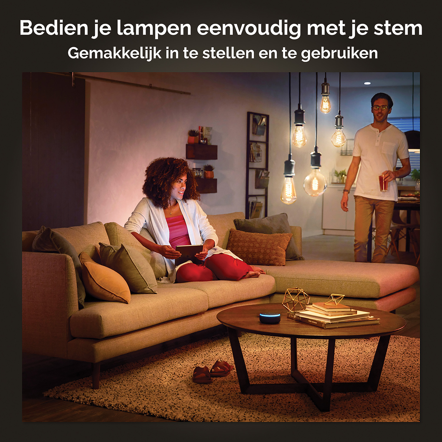 Vrouw op bank met tablet. Man met drankje. Hanglampen. Salontafel met items. Kamer met warme verlichting.