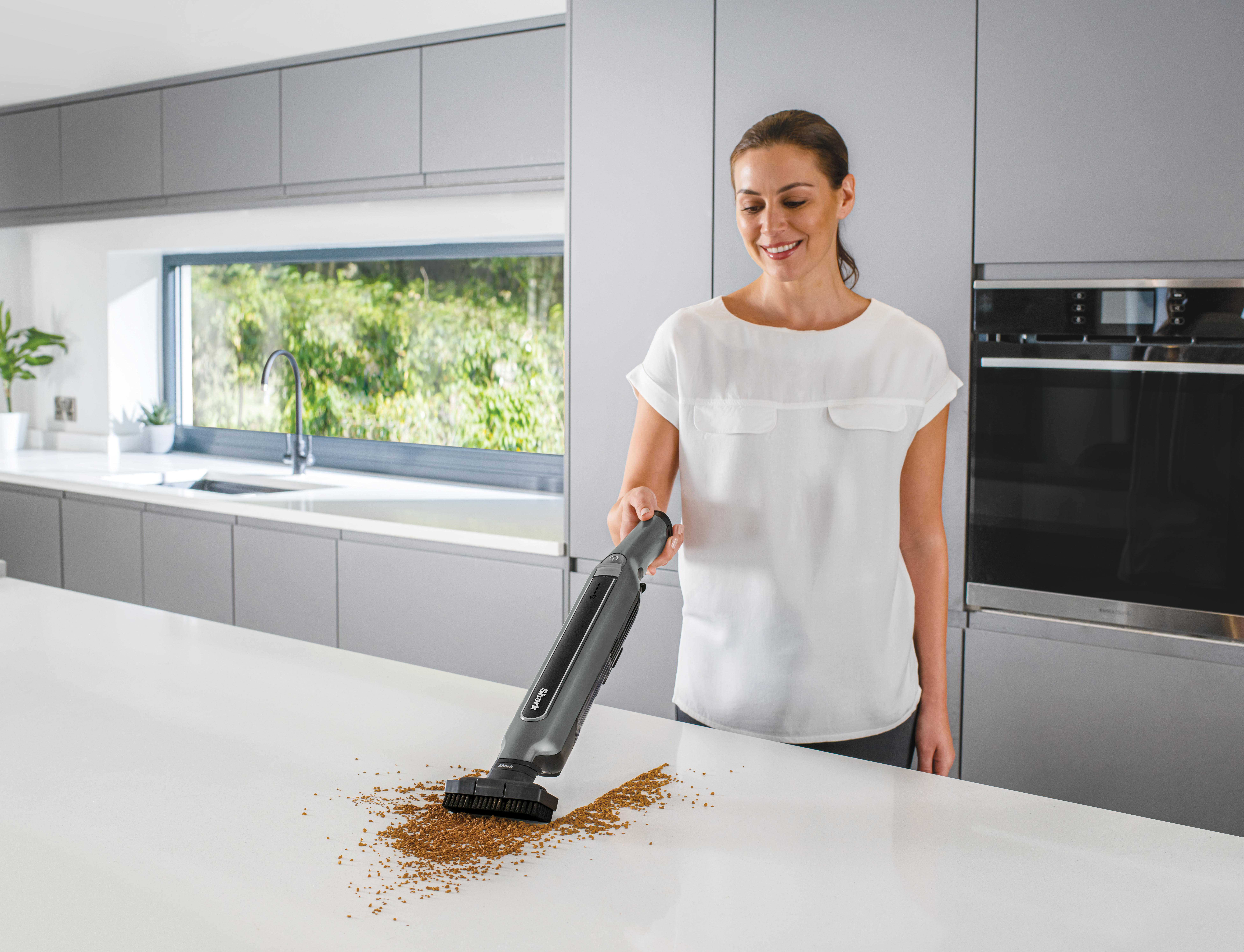 Frau, die eine weiße Arbeitsplatte mit einem grauen Staubsauger absaugt.