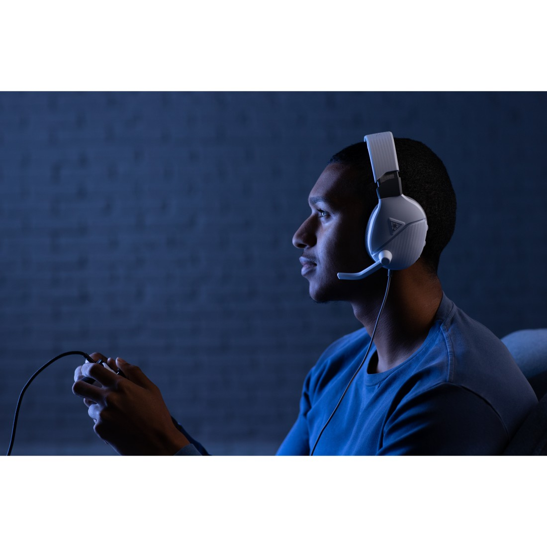 Mann mit weißem Gaming-Headset, spielt ein Spiel vor einer blau beleuchteten Wand.