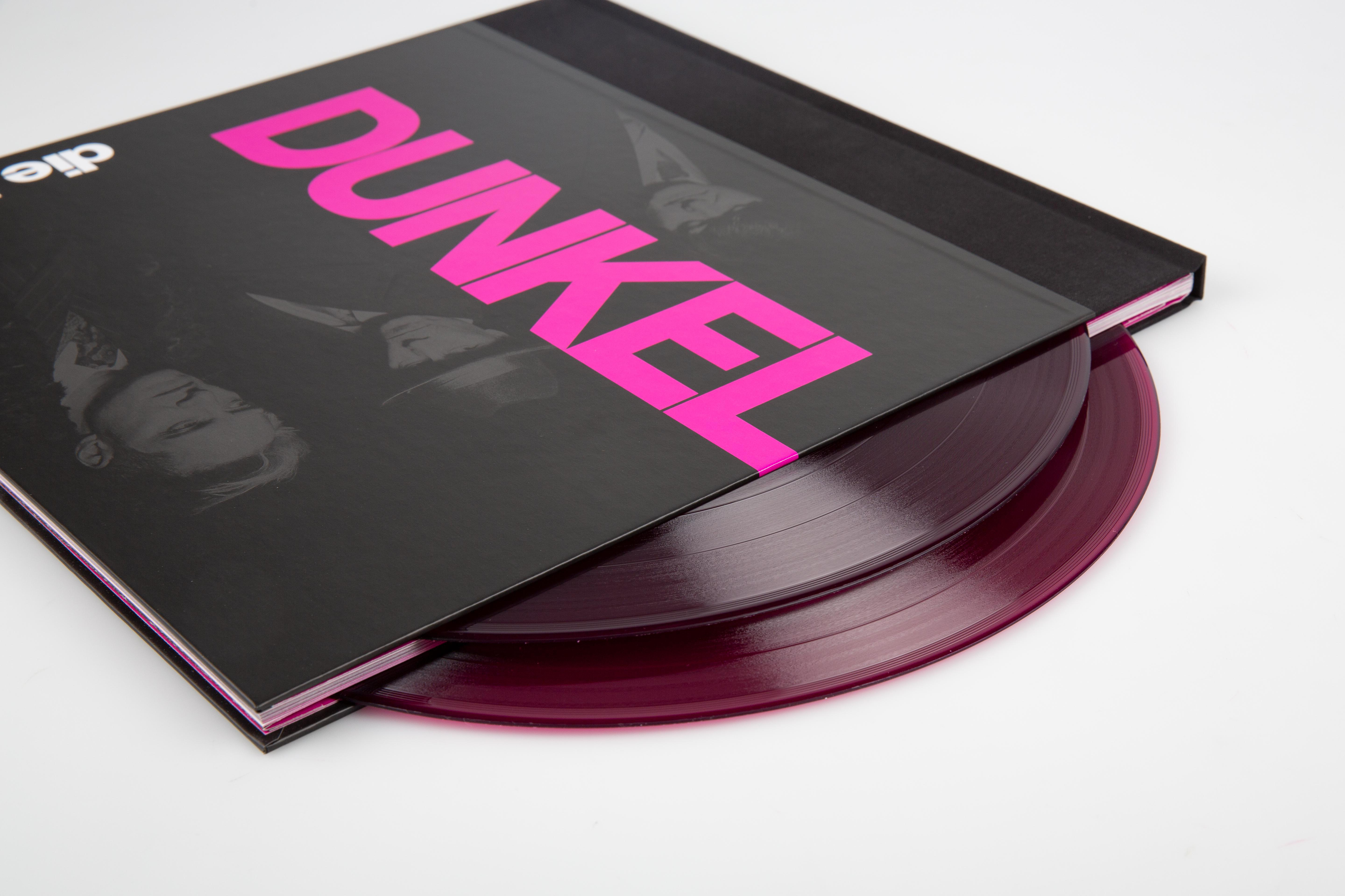 Ein Buch mit dem Wort 'DUNKEL' in Pink, mit zwei lila Schallplatten.