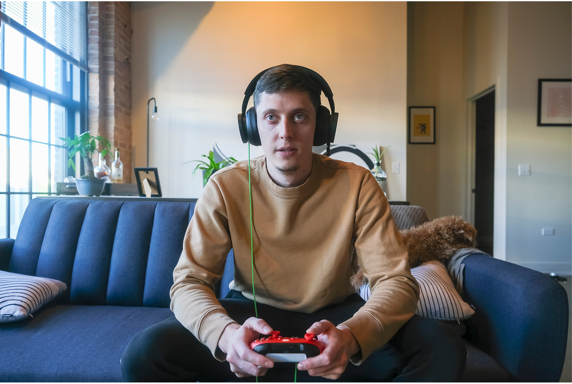 Un homme en pull beige jouant à un jeu, portant un casque, sur un canapé bleu.