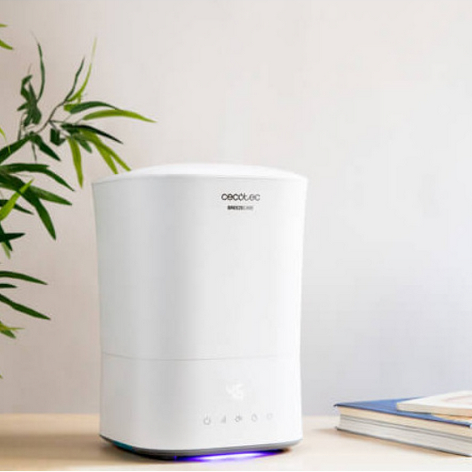 Un humidificador blanco con pantalla digital se sienta sobre una mesa junto a libros y plantas.