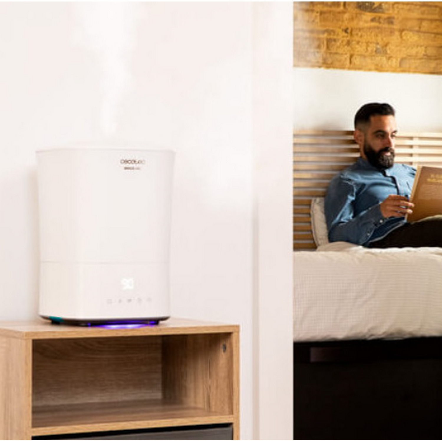 Un hombre lee un libro en la cama mientras un humidificador emite vapor.