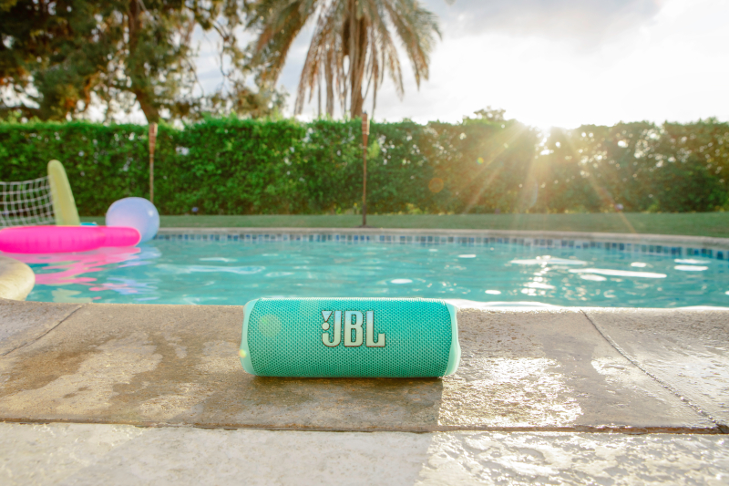 Ein JBL-Lautsprecher in der Nähe eines Pools, mit zwei Frauen im Hintergrund.