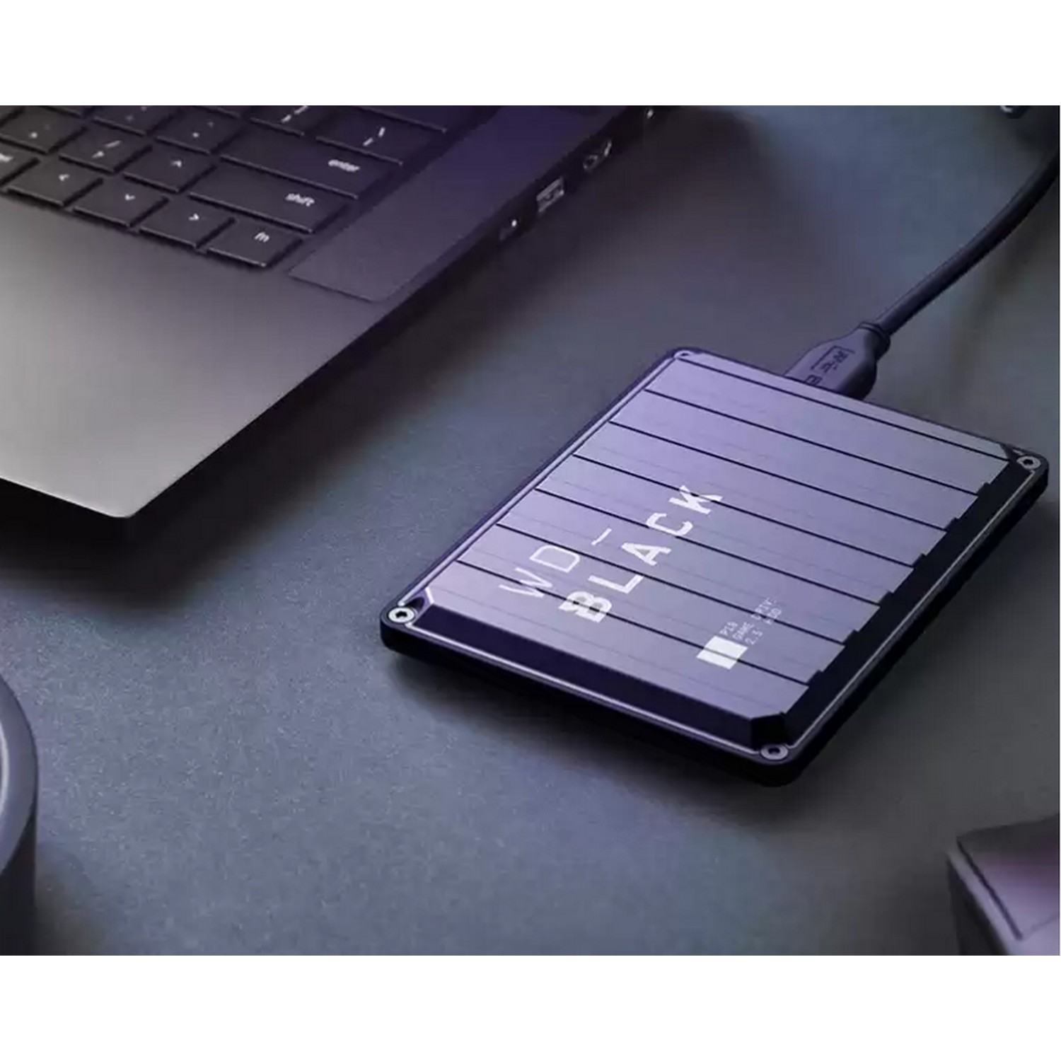 Disco duro externo WD negro conectado a un portátil en un escritorio oscuro.